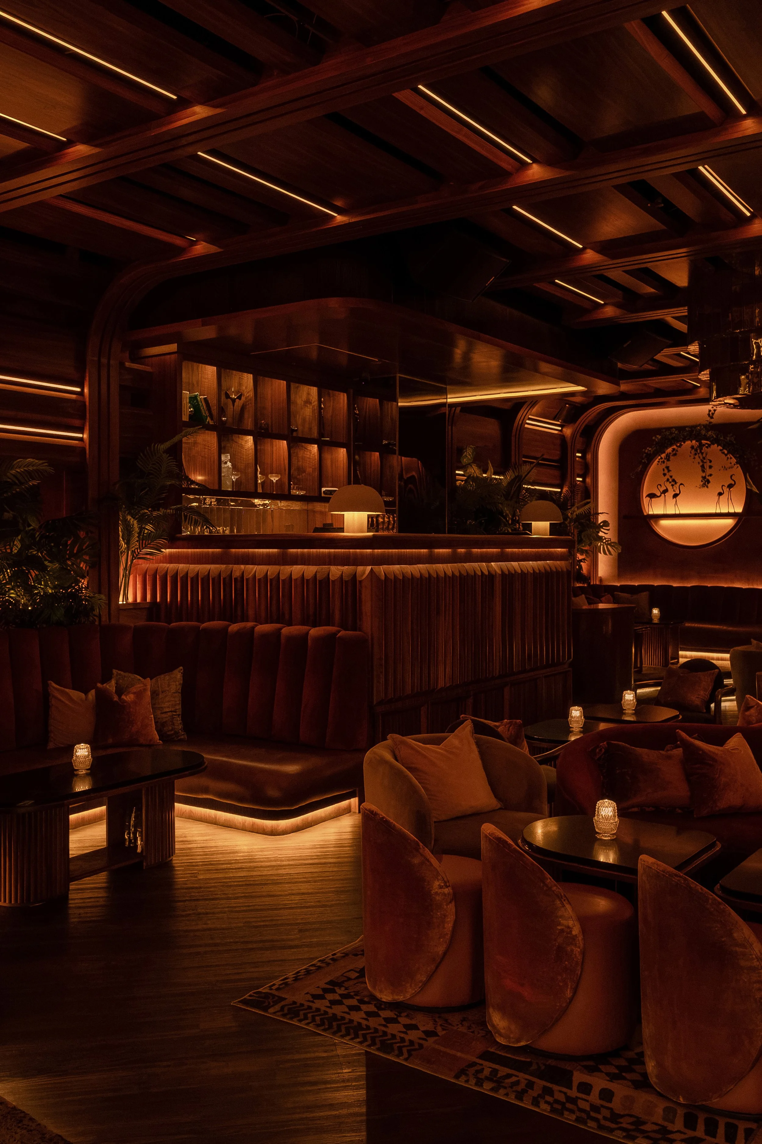 Plush seating area at Powder Room with curved banquettes, velvet lounge chairs and a warmly illuminated back bar.