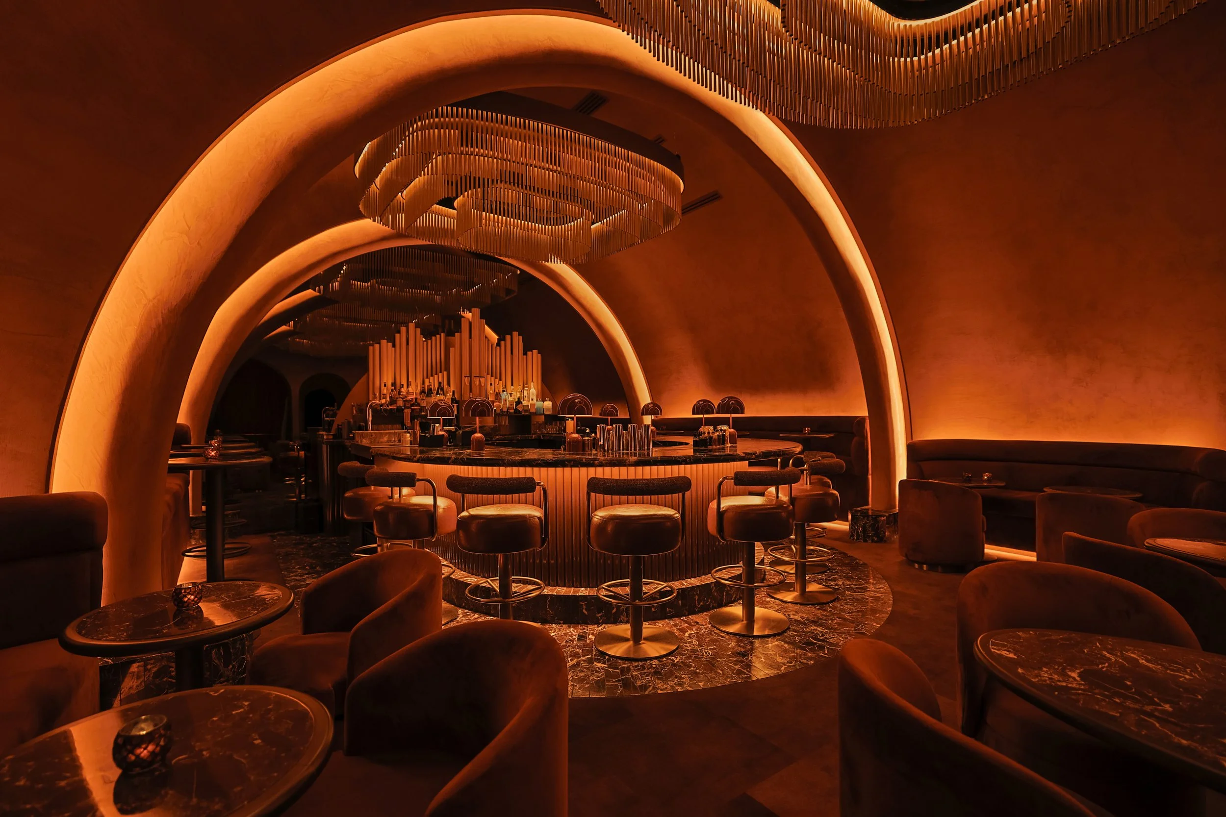 Wide diagonal view of Mea Culpa’s vaulted cocktail lounge, featuring intimate seating, a marble bar and an organ-inspired installation.
