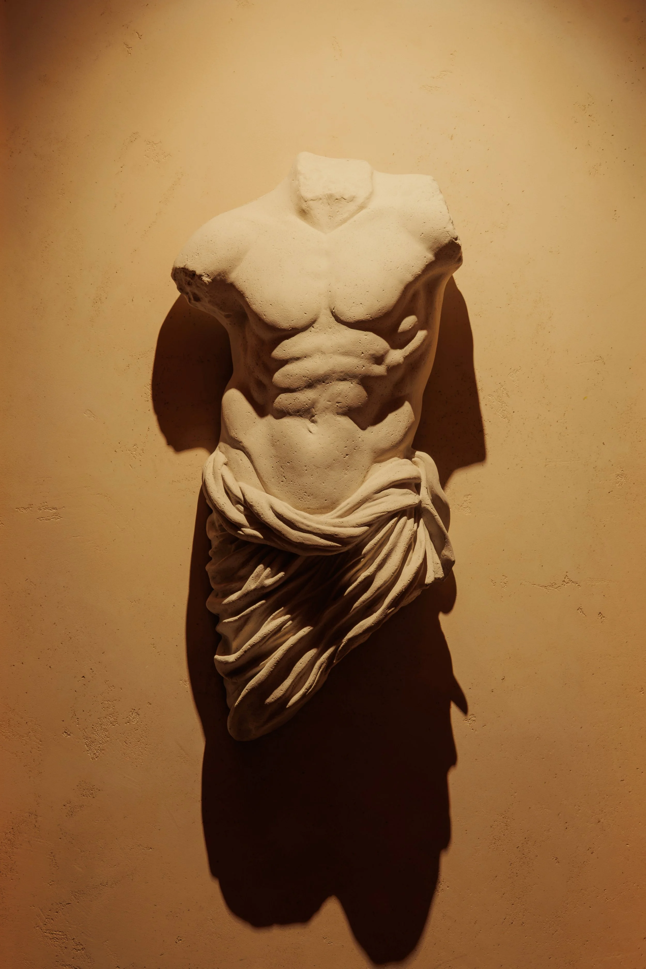 Close-up of a headless classical male torso draped in sculpted fabric and dramatically illuminated at Roman God of Fire in Tempe.