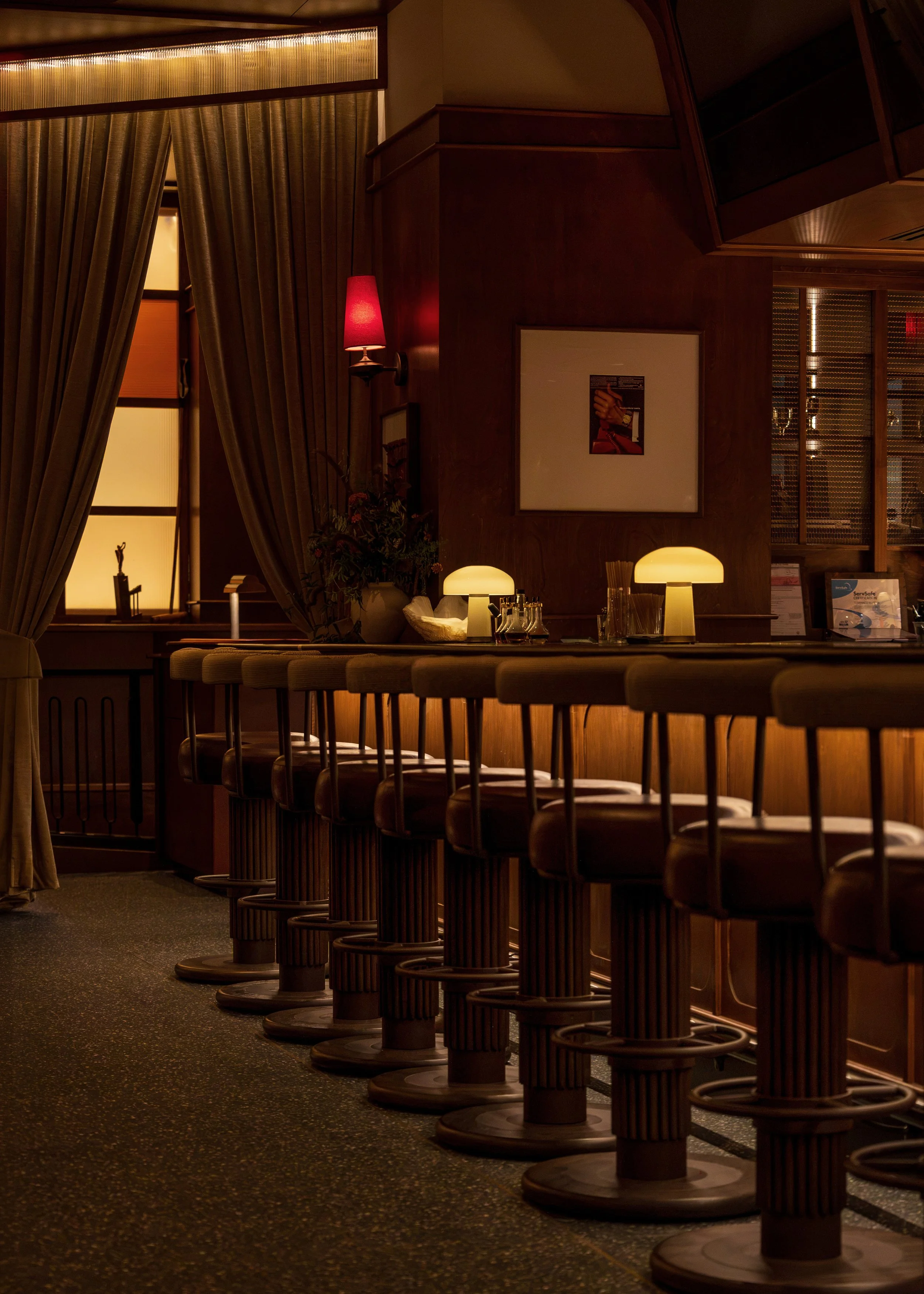 Leather bar stools, shaded table lamps and a softly glowing back bar reinforce the atmosphere of a private members’ club.