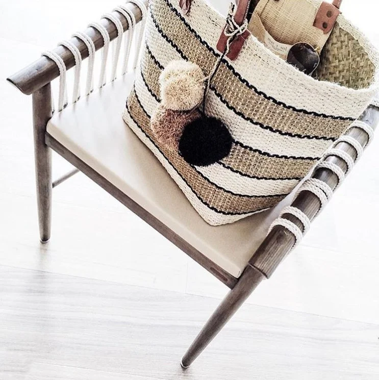 Decorative striped handbag on a white seat bench with a pom-pom keychain hanging from it.