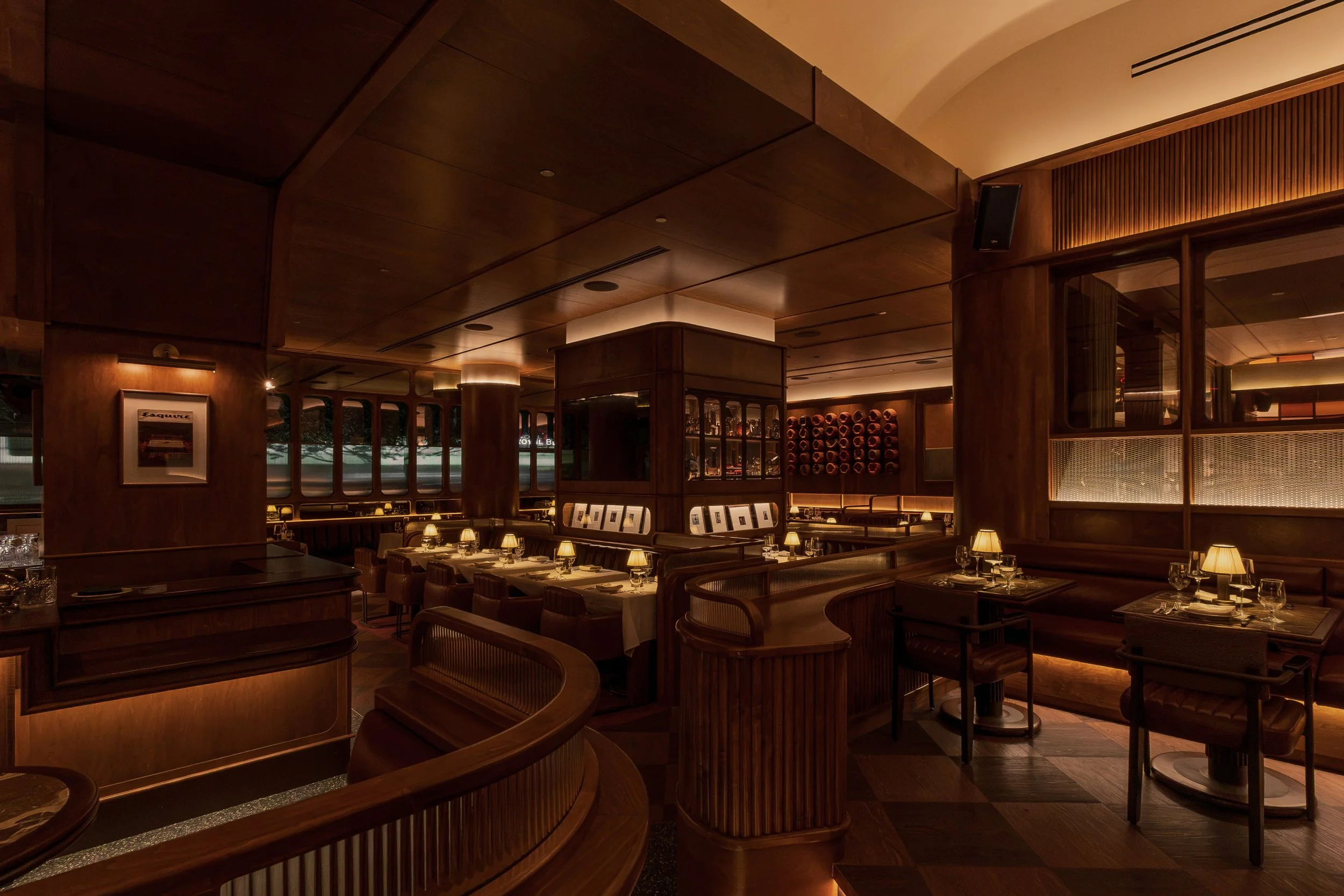 Wide view of Austin Sports Club’s central bar and surrounding dining areas, layered with curved millwork, leather seating and warm architectural lighting.