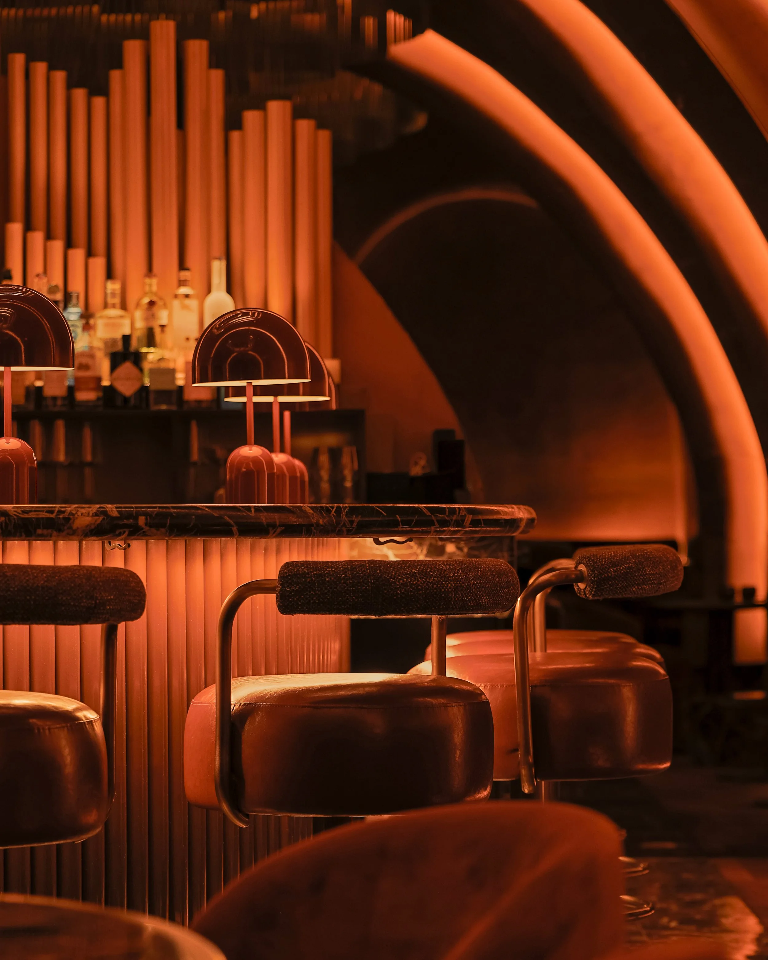 Close-up of Mea Culpa’s upholstered bar stools, fluted illuminated millwork, red dome lamps and organ-inspired bar installation.