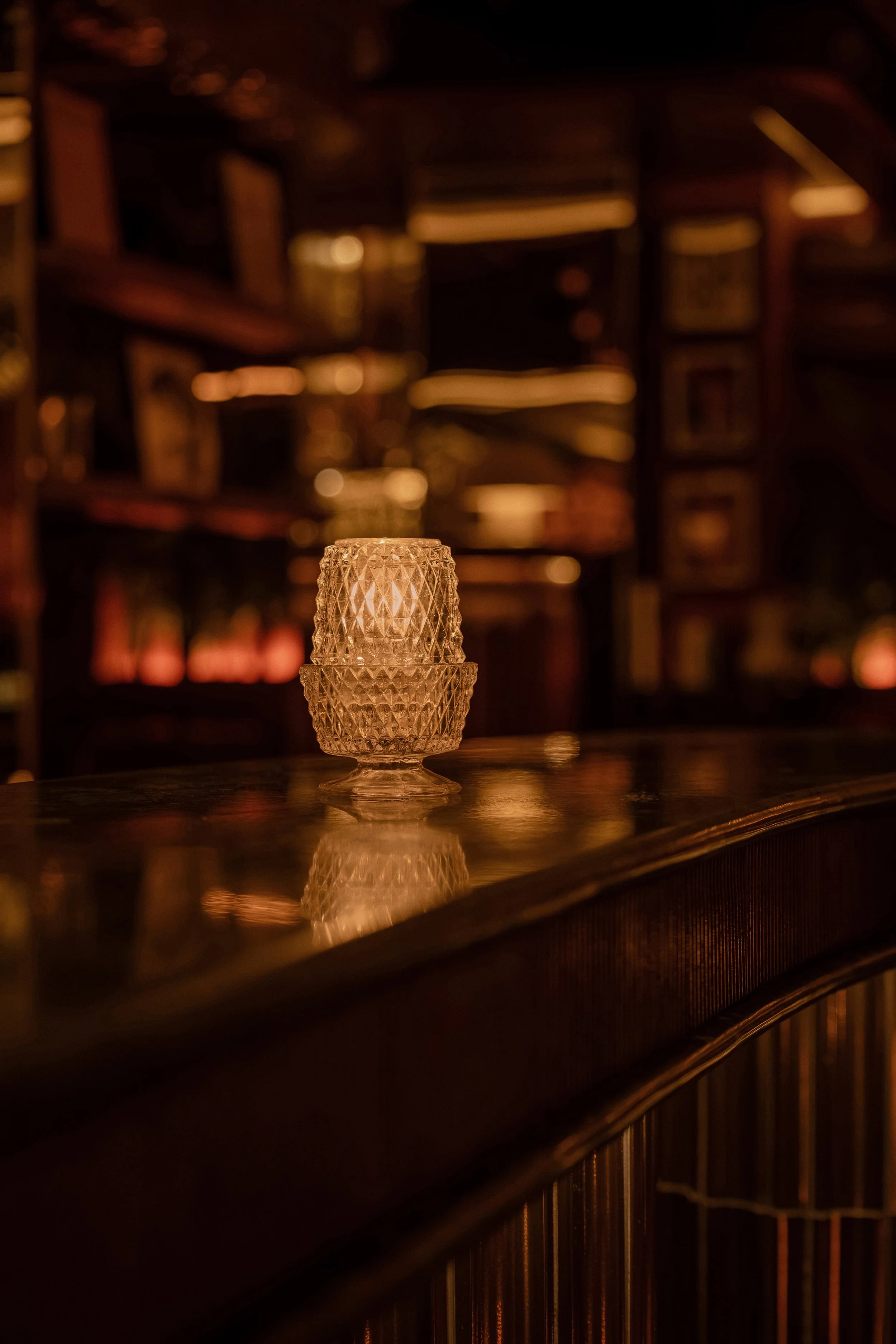 Close-up of a faceted glass table lamp reflected in the polished bar surface at Powder Room.