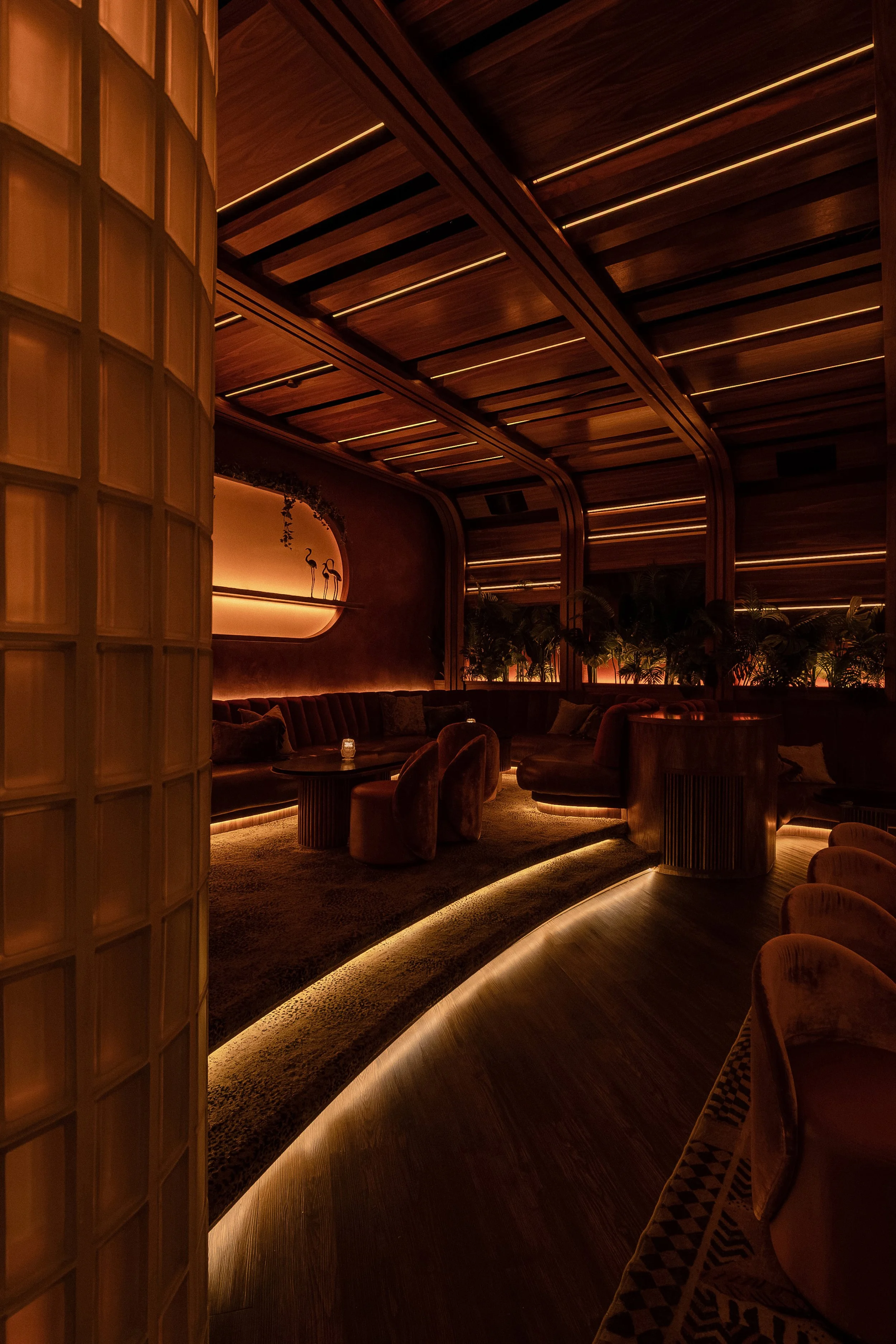 Glowing curved steps and glass-block column marking the transition into Powder Room’s intimate seating area.