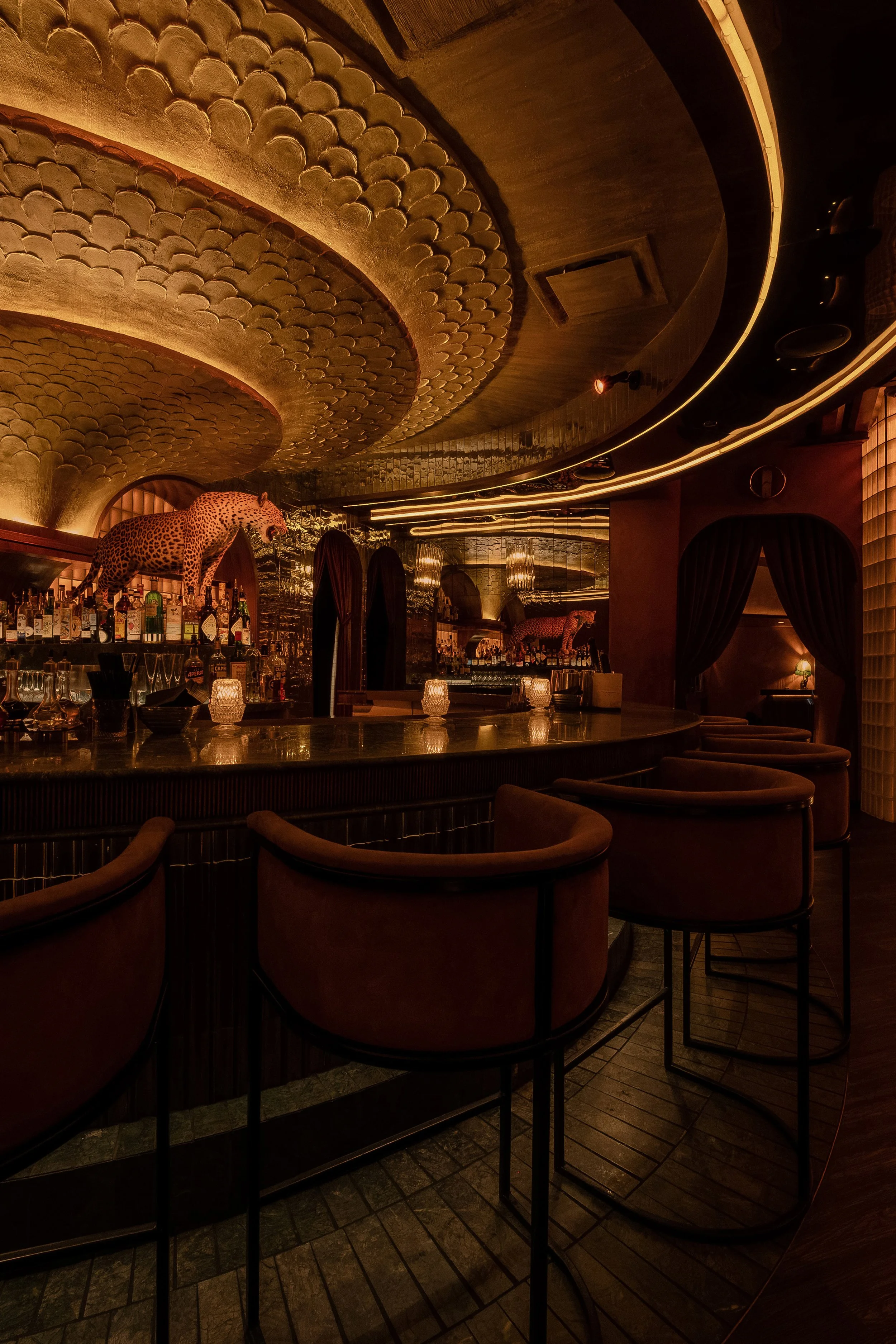 Vertical view of Powder Room’s bar seating beneath its carved, illuminated ceiling with a leopard sculpture above the back bar.