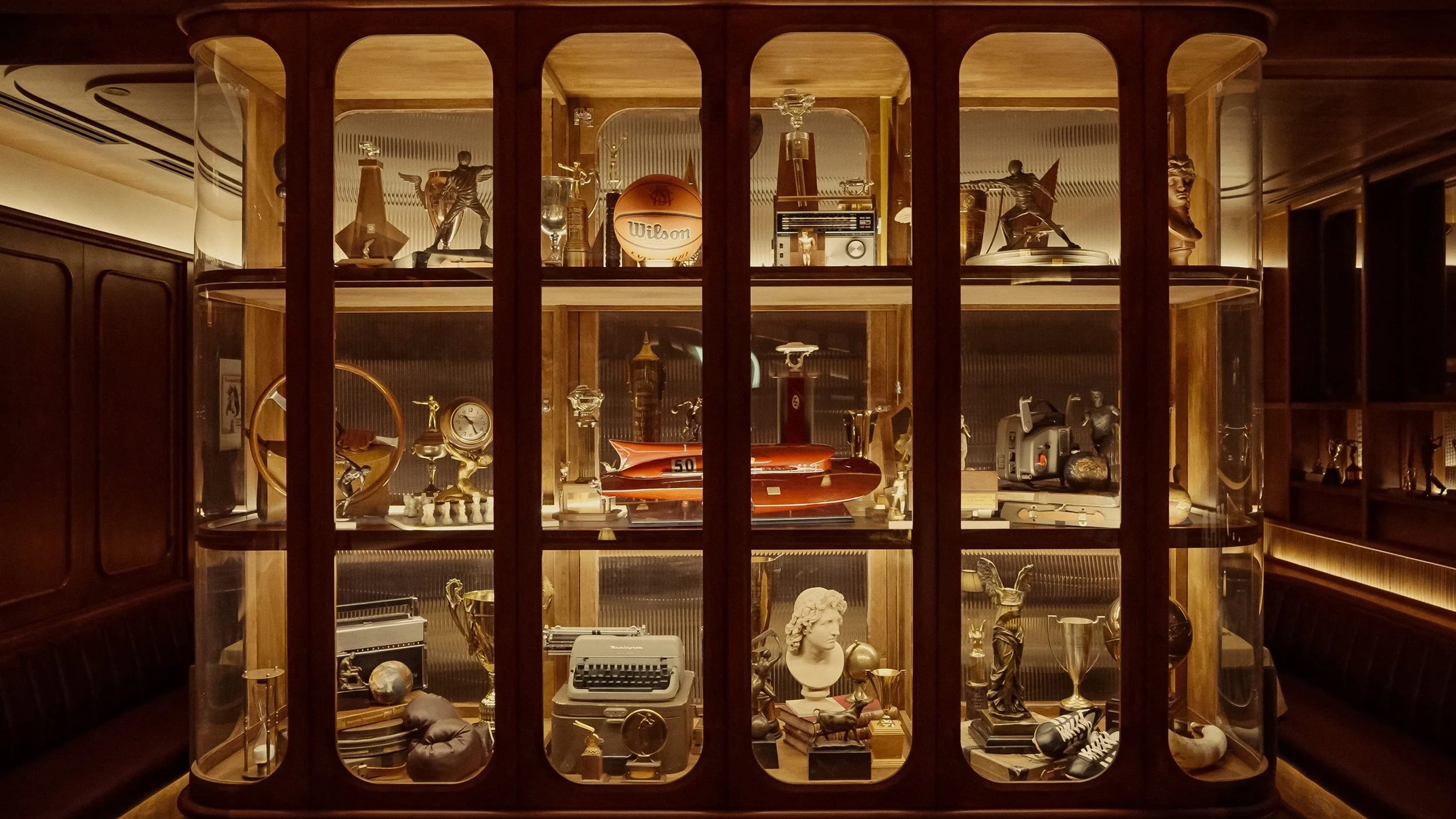 Custom wood-and-glass display cabinets showcase trophies, photographs and vintage sporting objects collected throughout the club.