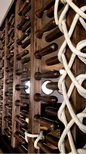 A wine rack with multiple bottles stored horizontally and a climbing rope tied to it.