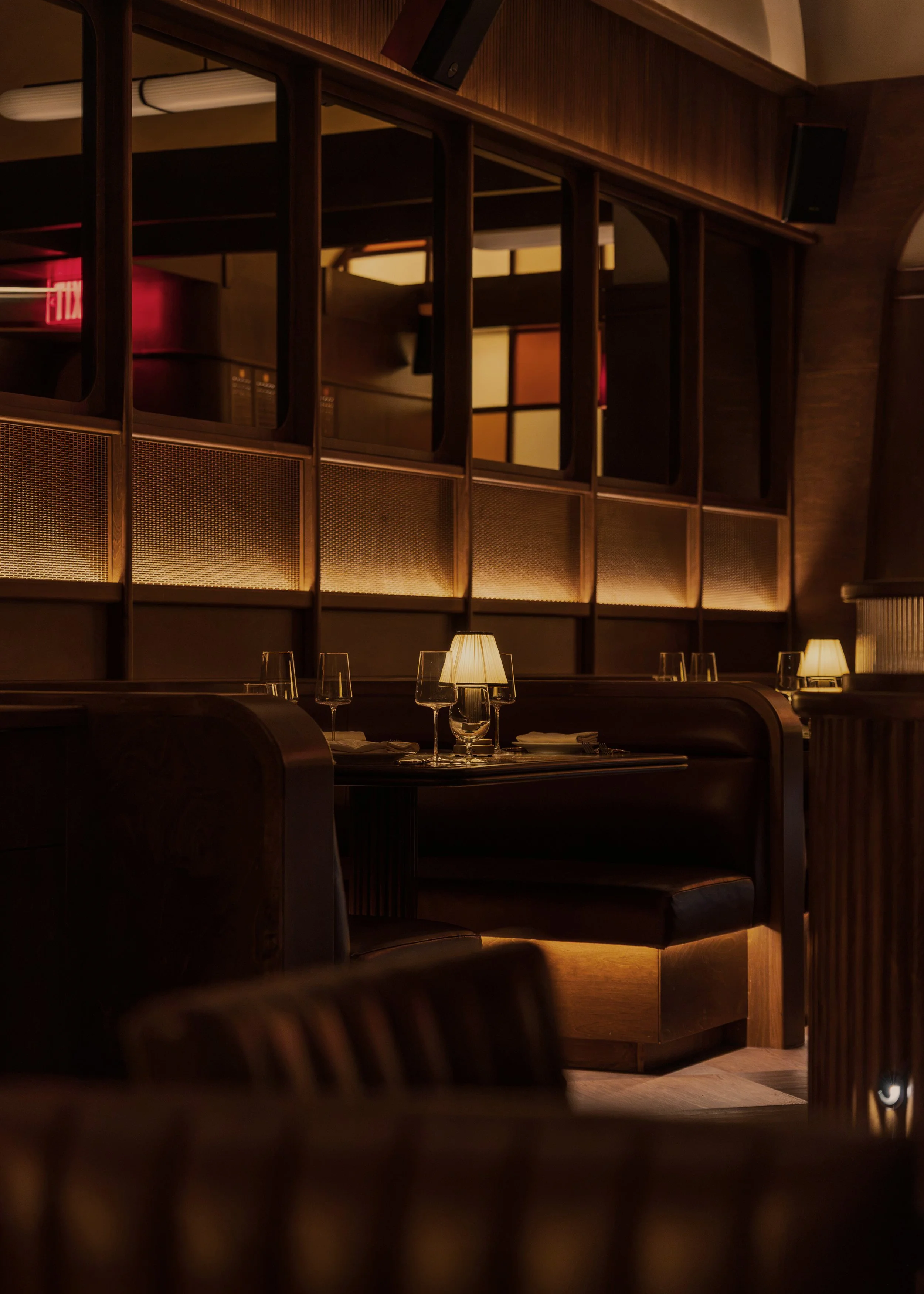 Intimate leather booths sit beneath decorative metal screens and interior windows that connect the club’s layered spaces.