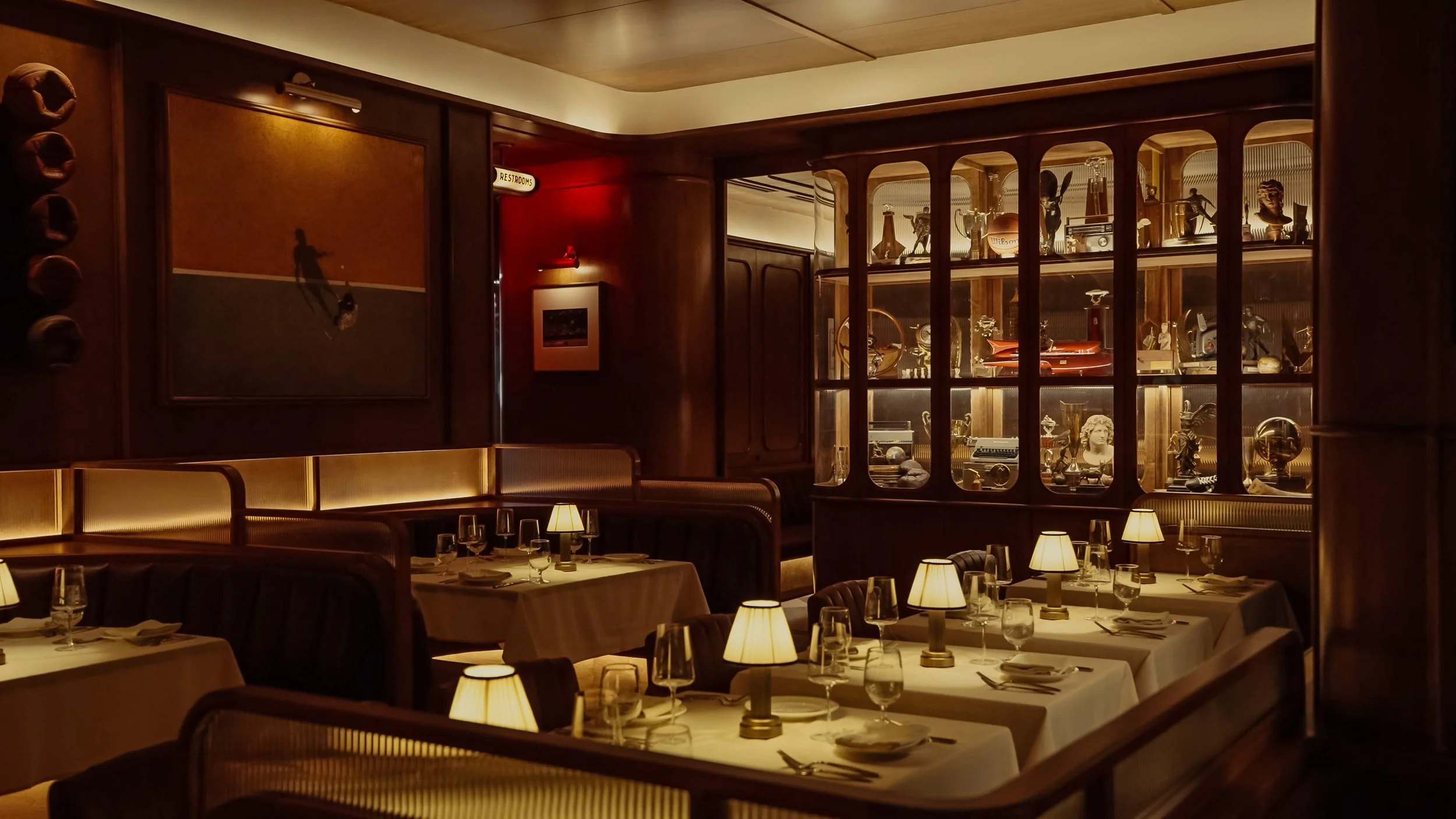 Austin Sports Club’s dining room combines white table settings, leather seating and illuminated cabinets displaying curated athletic artifacts.
