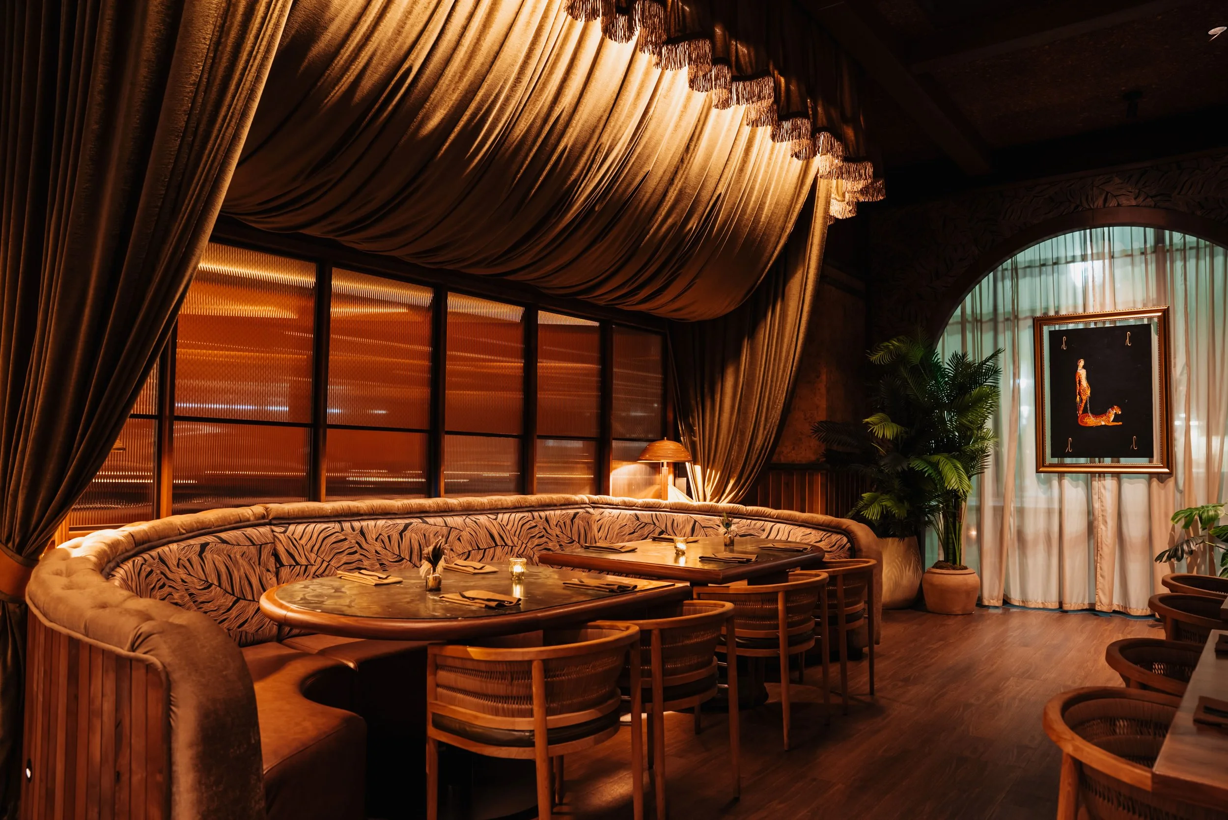 Jungle-inspired dining room at Filthy Animal in Tempe, featuring deep green leather seating, tropical plants, warm wood finishes, richly textured surfaces and dramatic animal imagery.