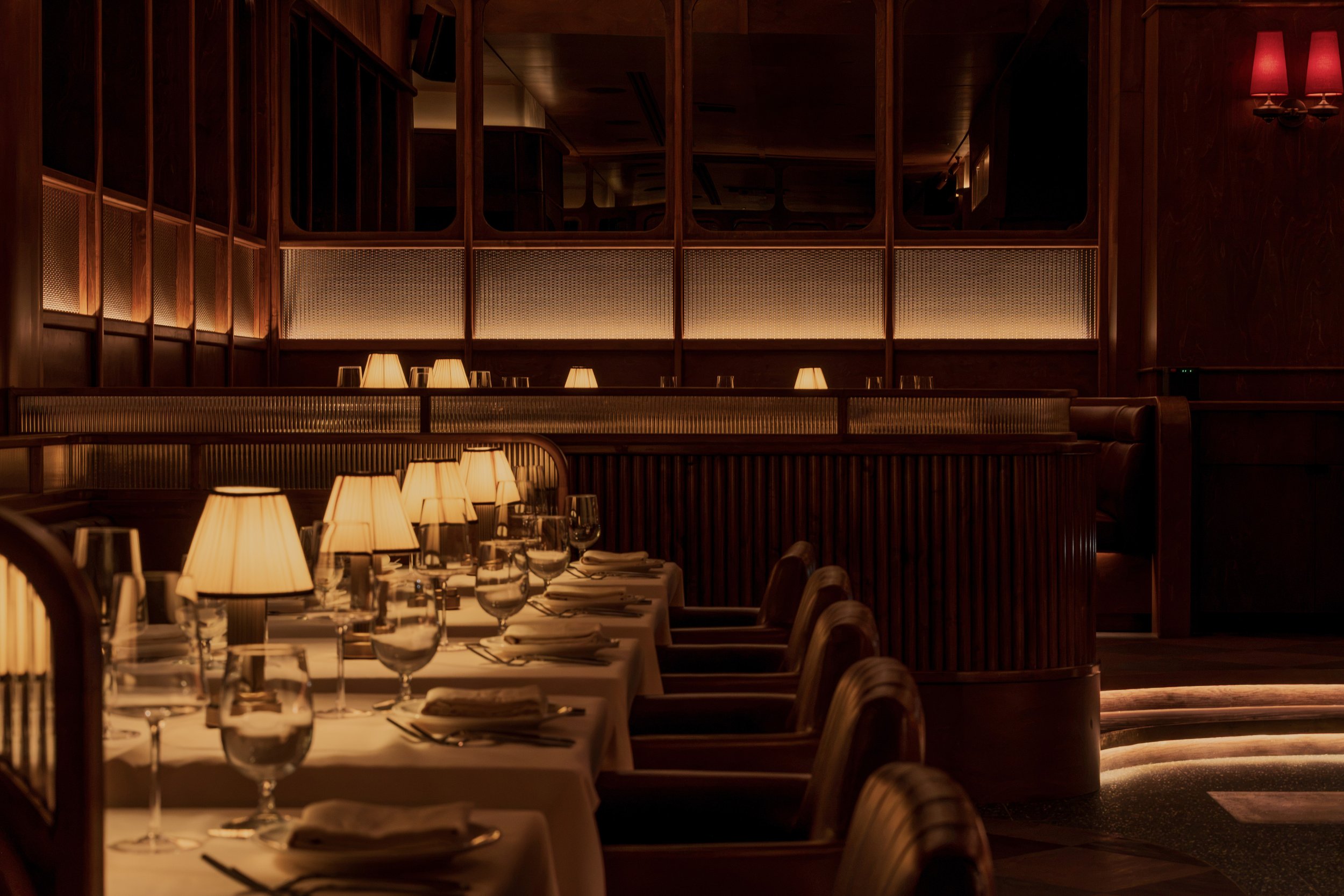A formal dining table runs alongside ribbed wood paneling, leather chairs and softly glowing architectural screens.