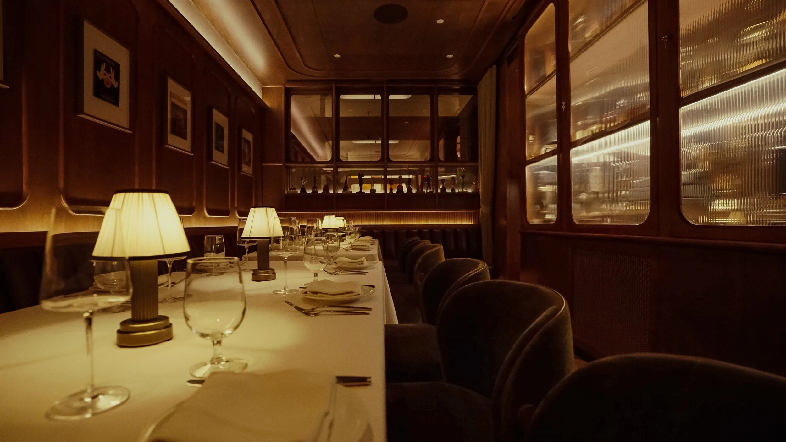 A formal dining table runs alongside ribbed wood paneling, leather chairs and softly glowing architectural screens.