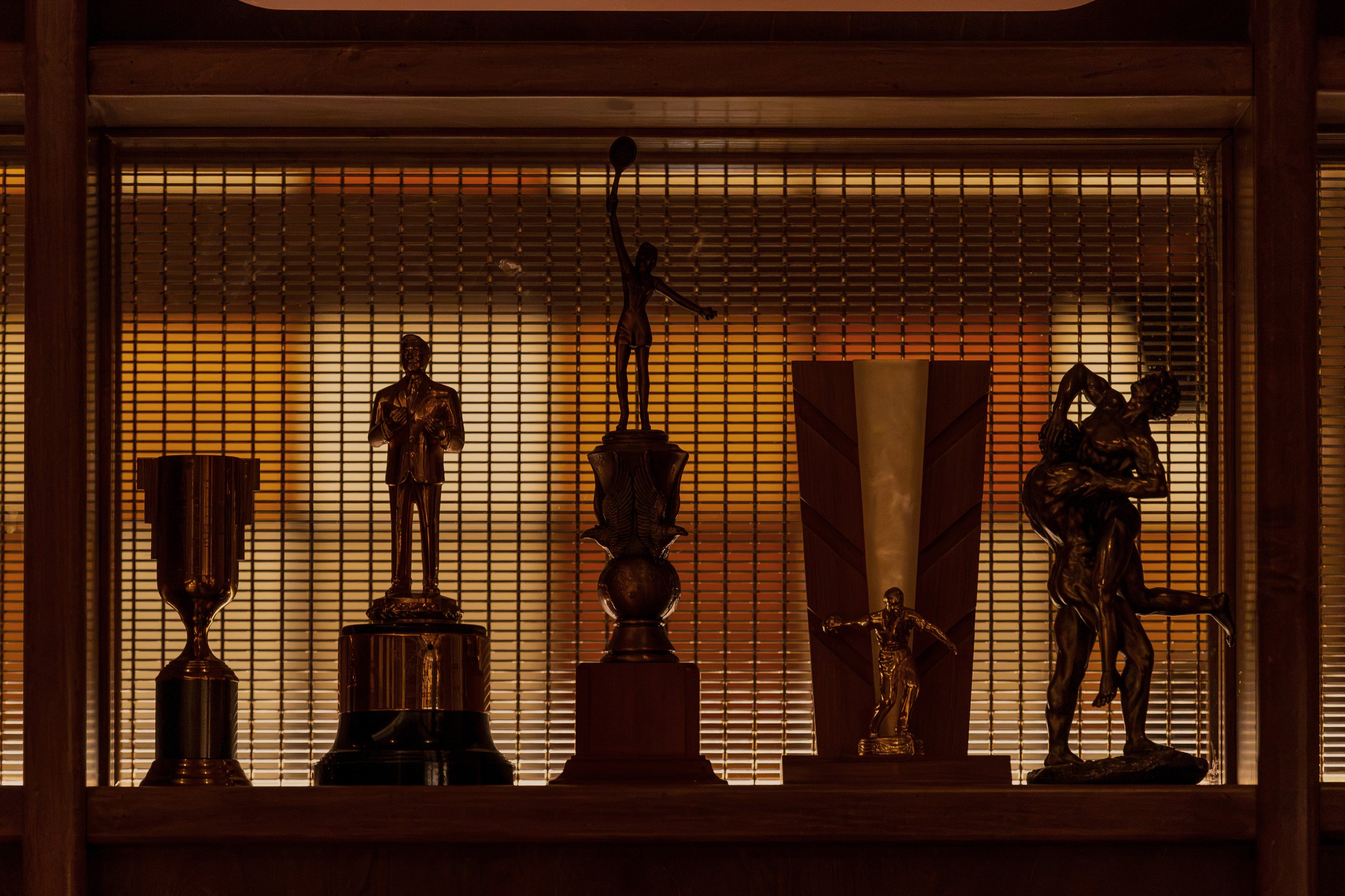Athlete sculptures appear in silhouette against an amber backlit screen, creating a museum-like display of sporting history.