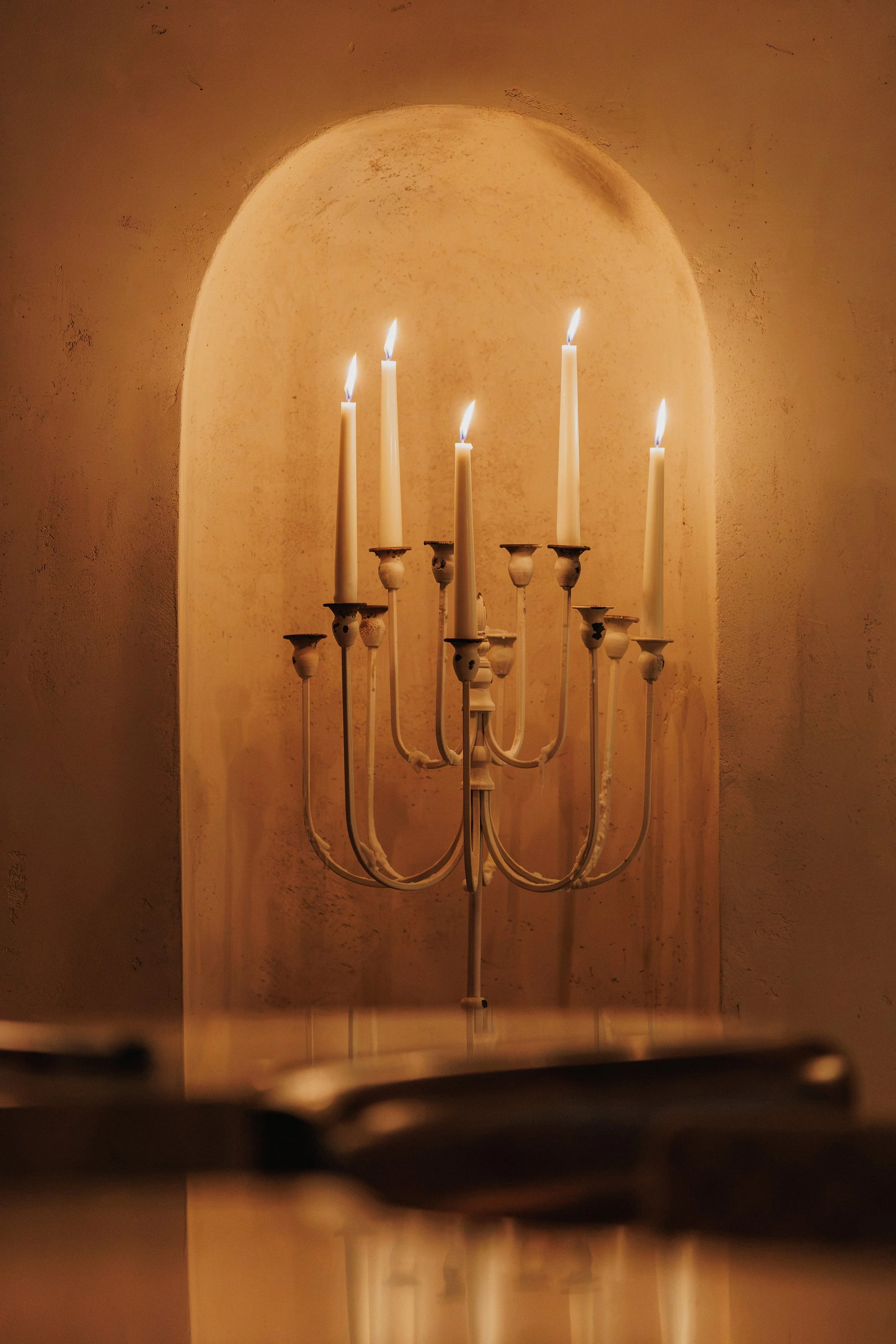 Traditional brass candelabra with lit taper candles displayed within a softly illuminated arched wall niche.