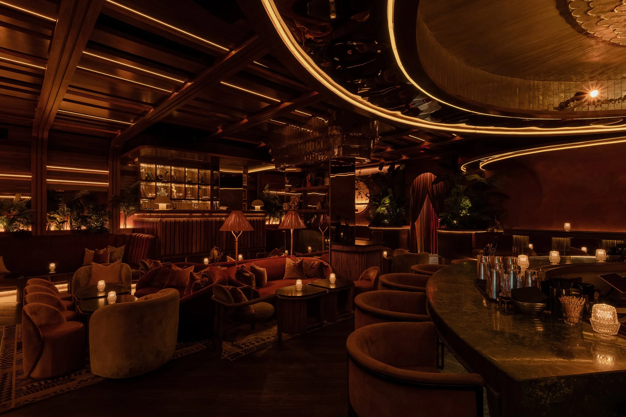 Sweeping view of Powder Room’s lounge with curved banquettes, velvet seating, candlelit tables and sculptural ceiling lighting.