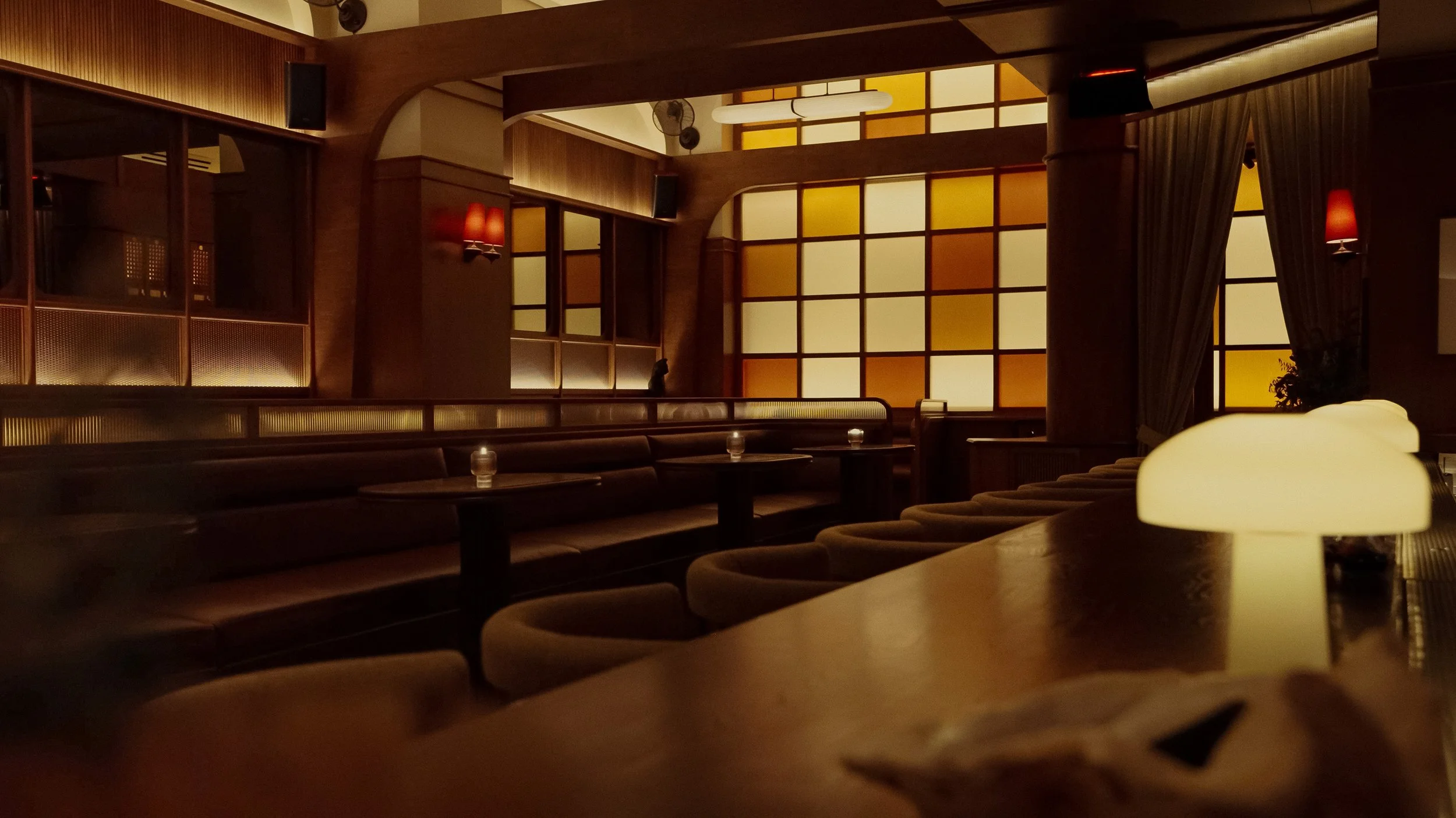 A softly glowing wall of amber glass blocks forms the backdrop for dark leather banquettes and intimate dining tables.
