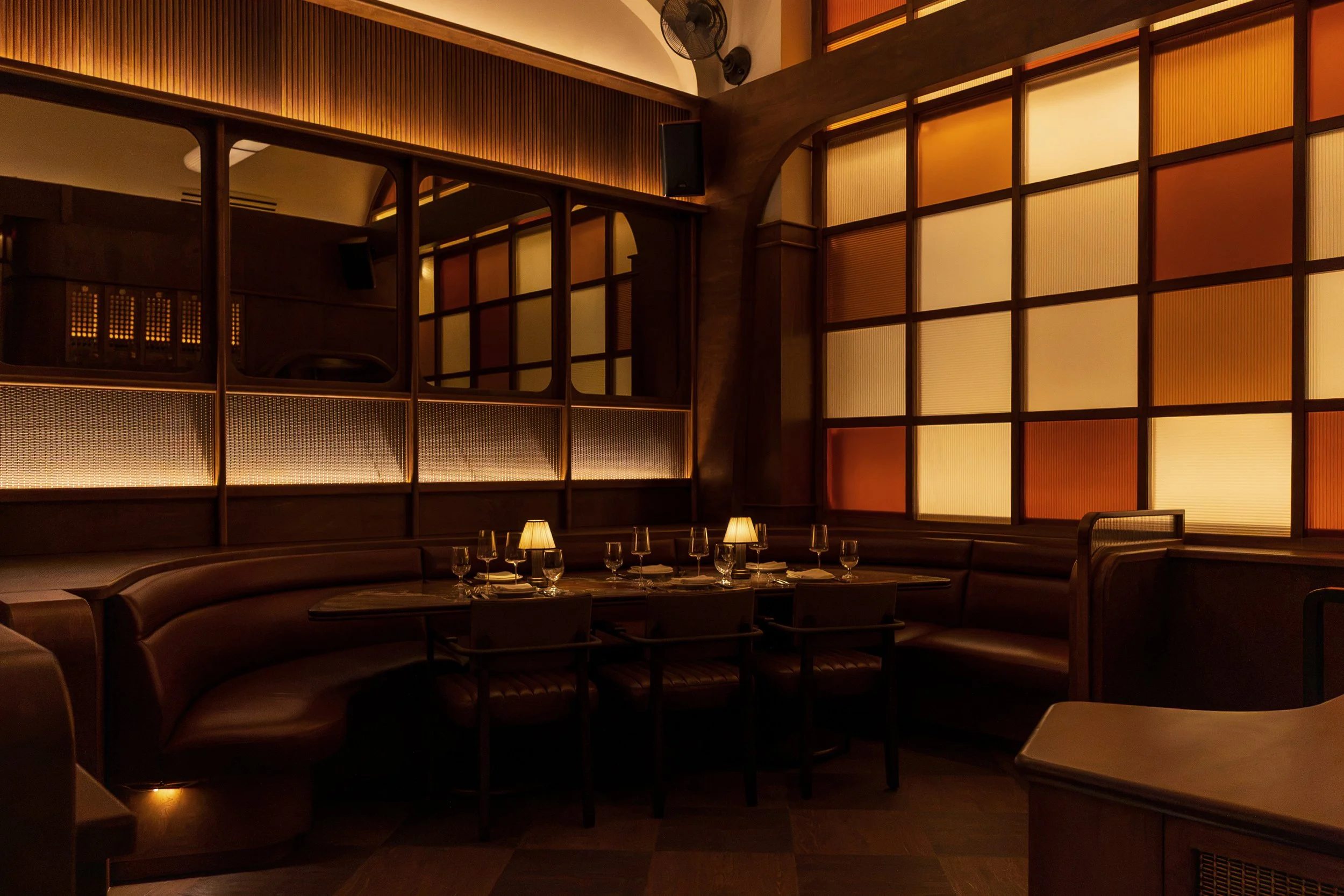 An intimate dining area features dark leather seating, candlelit tables and amber-glazed windows that cast a warm evening glow.