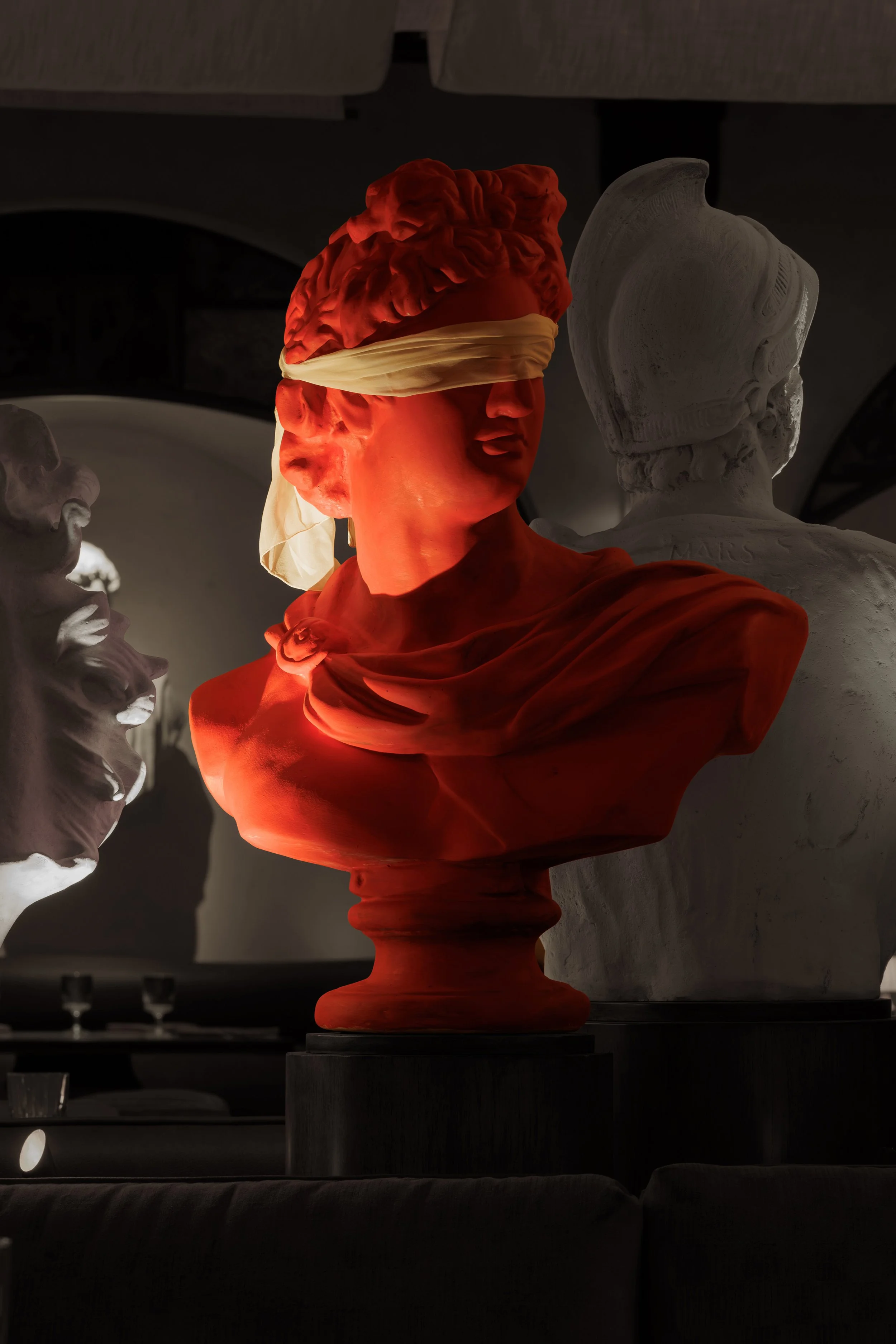 Red classical bust dramatically illuminated in front of layered stone sculptures within the restaurant’s art installation.