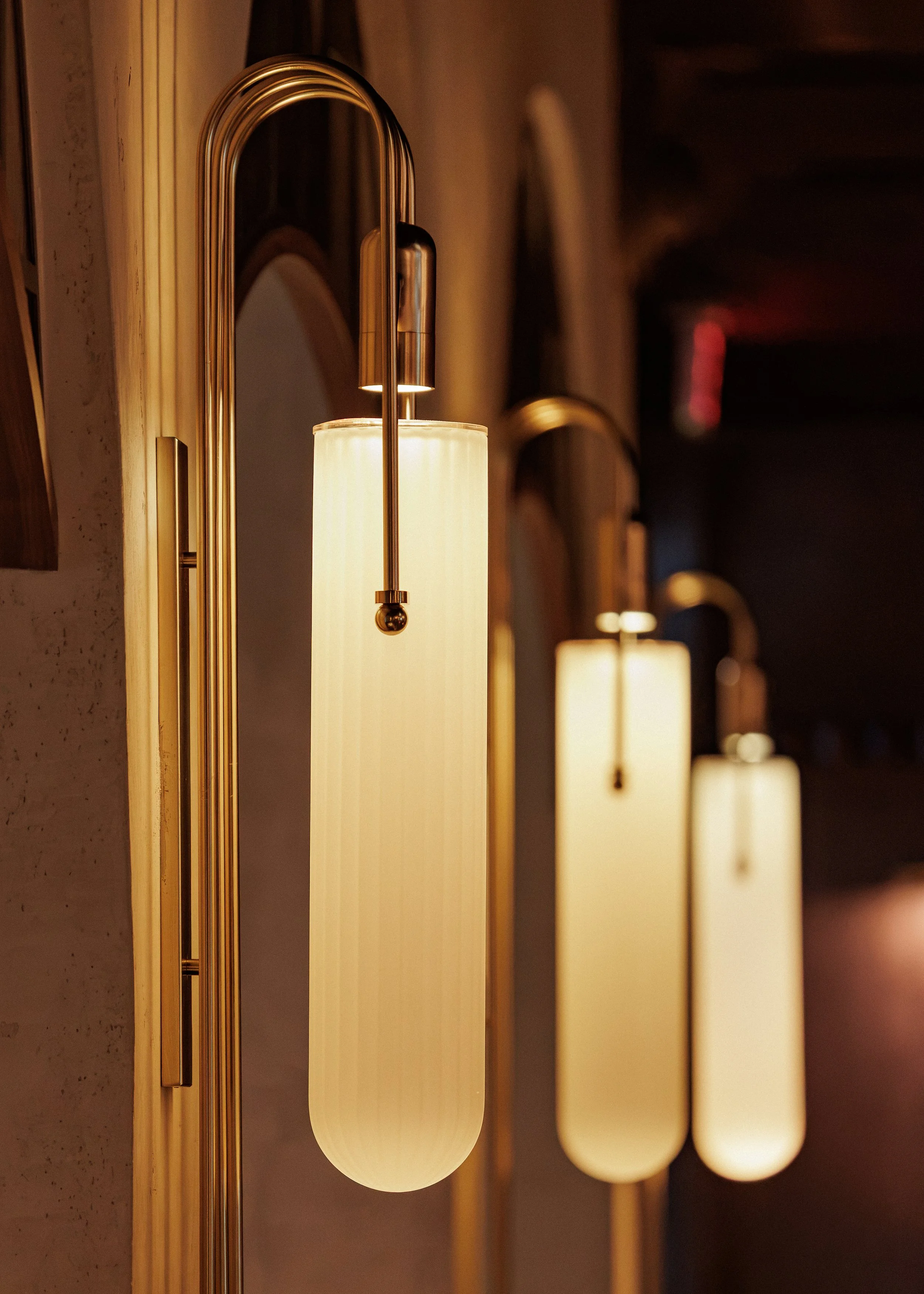 Art Deco-inspired wall sconces with elongated illuminated glass shades and polished brass frames inside Roman God of Fire.