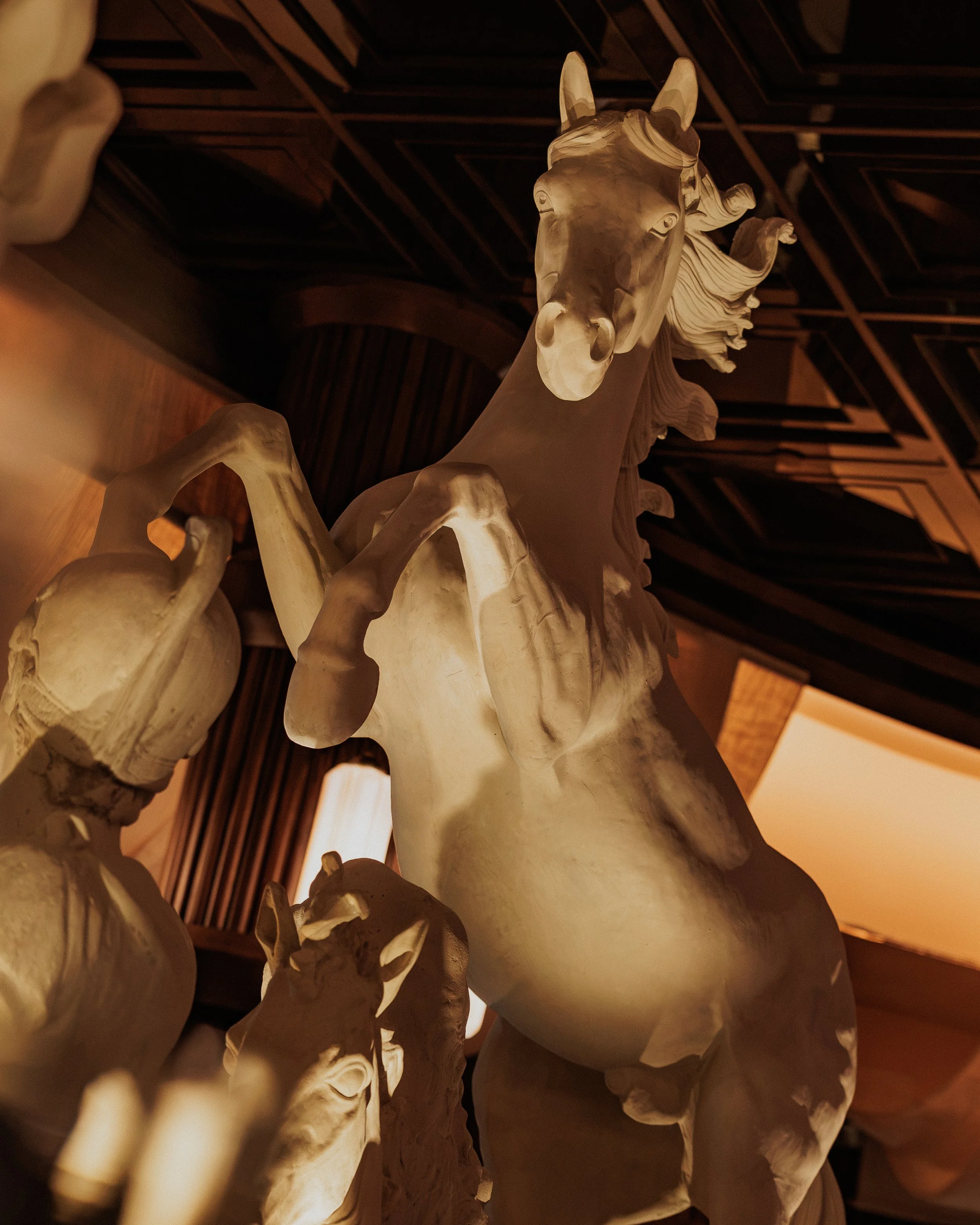 Close view of illuminated classical horse sculptures displayed beneath the dark coffered ceiling at Roman God of Fire.
