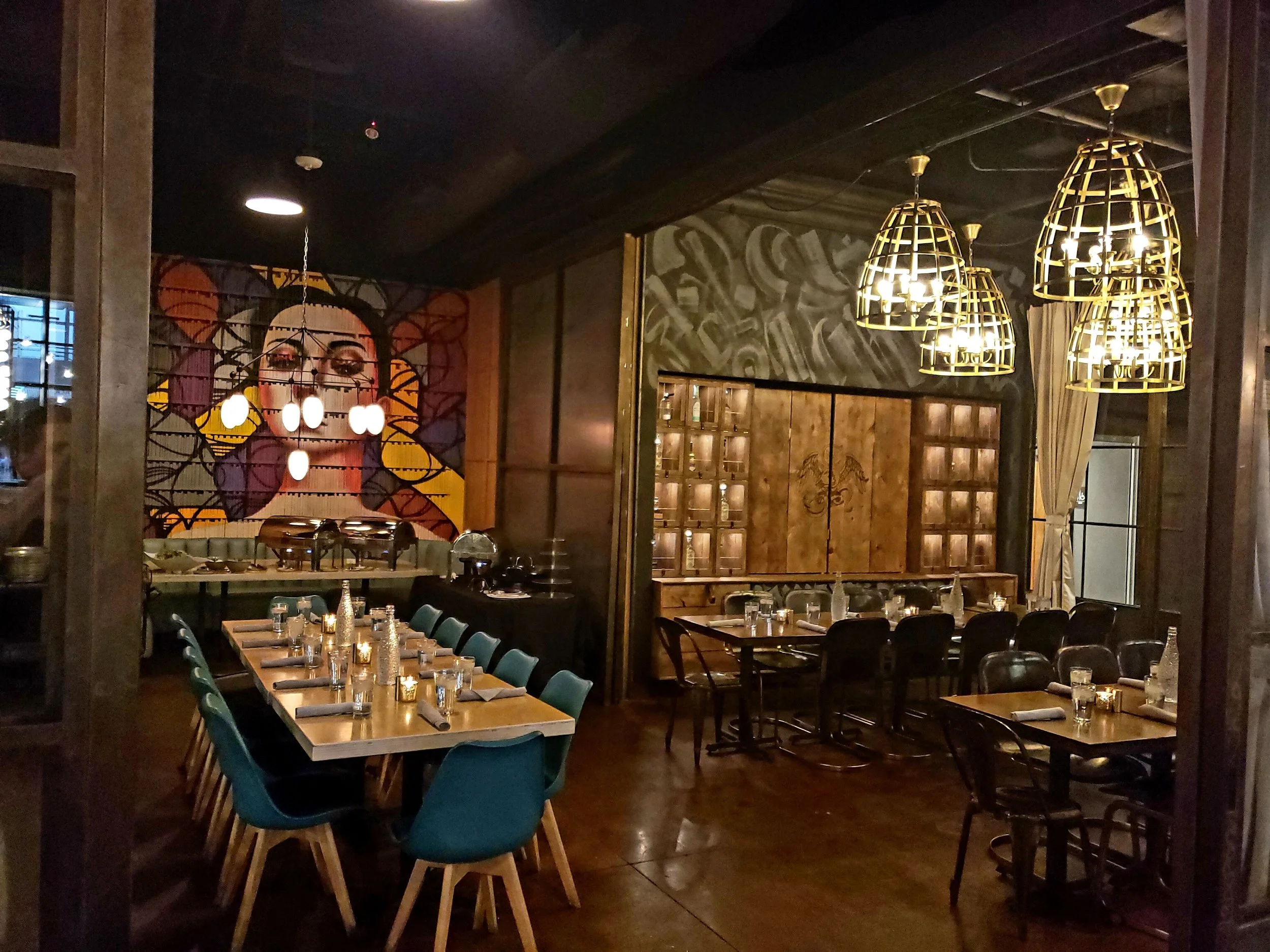Chico Malo restaurant interior in Downtown Phoenix, featuring dark wood paneling, colorful artwork, woven pendant lights, teal dining chairs, and intimate dining spaces.