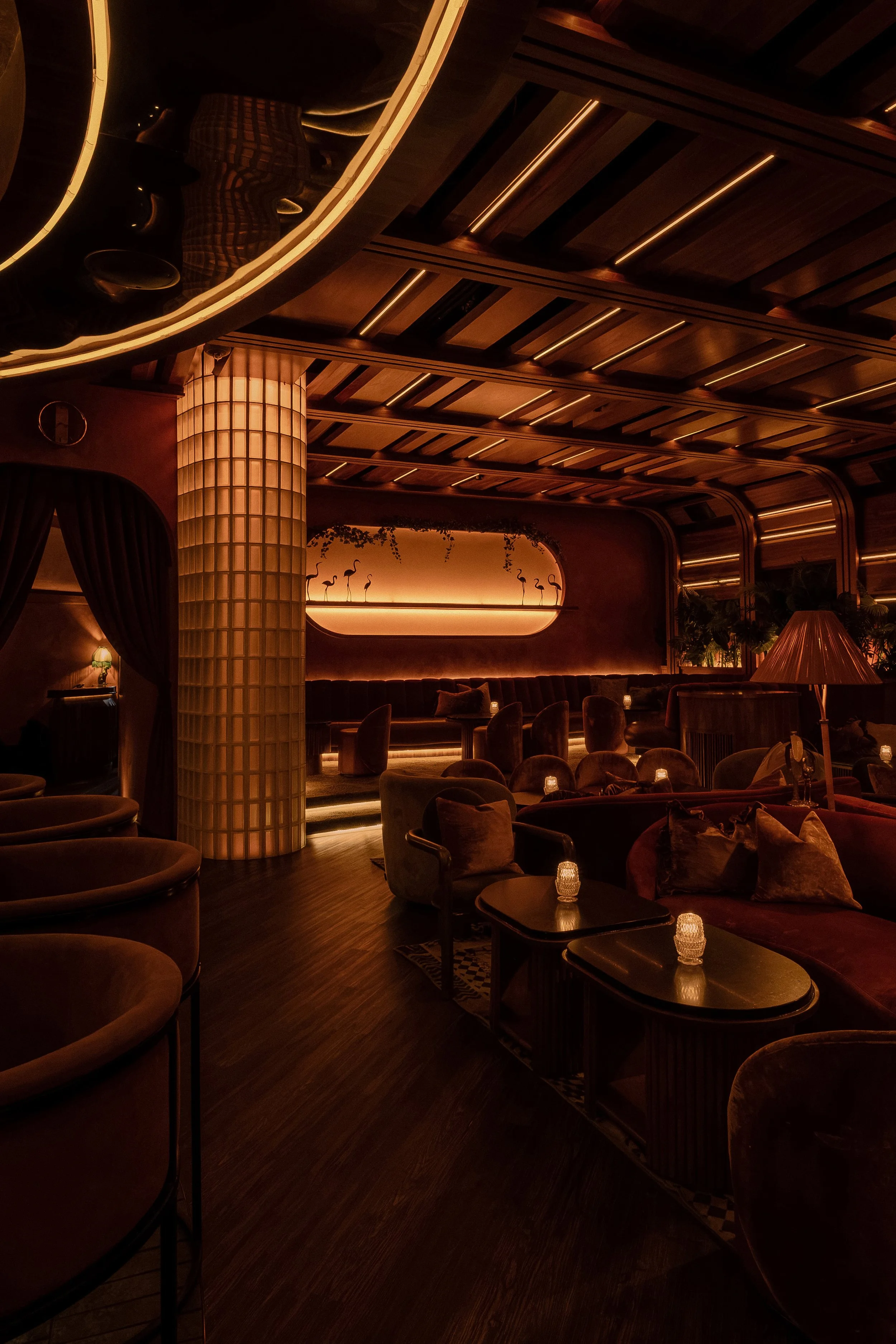 Interior view of Powder Room featuring a glowing glass-block column, layered wood ceiling and intimate cocktail seating.