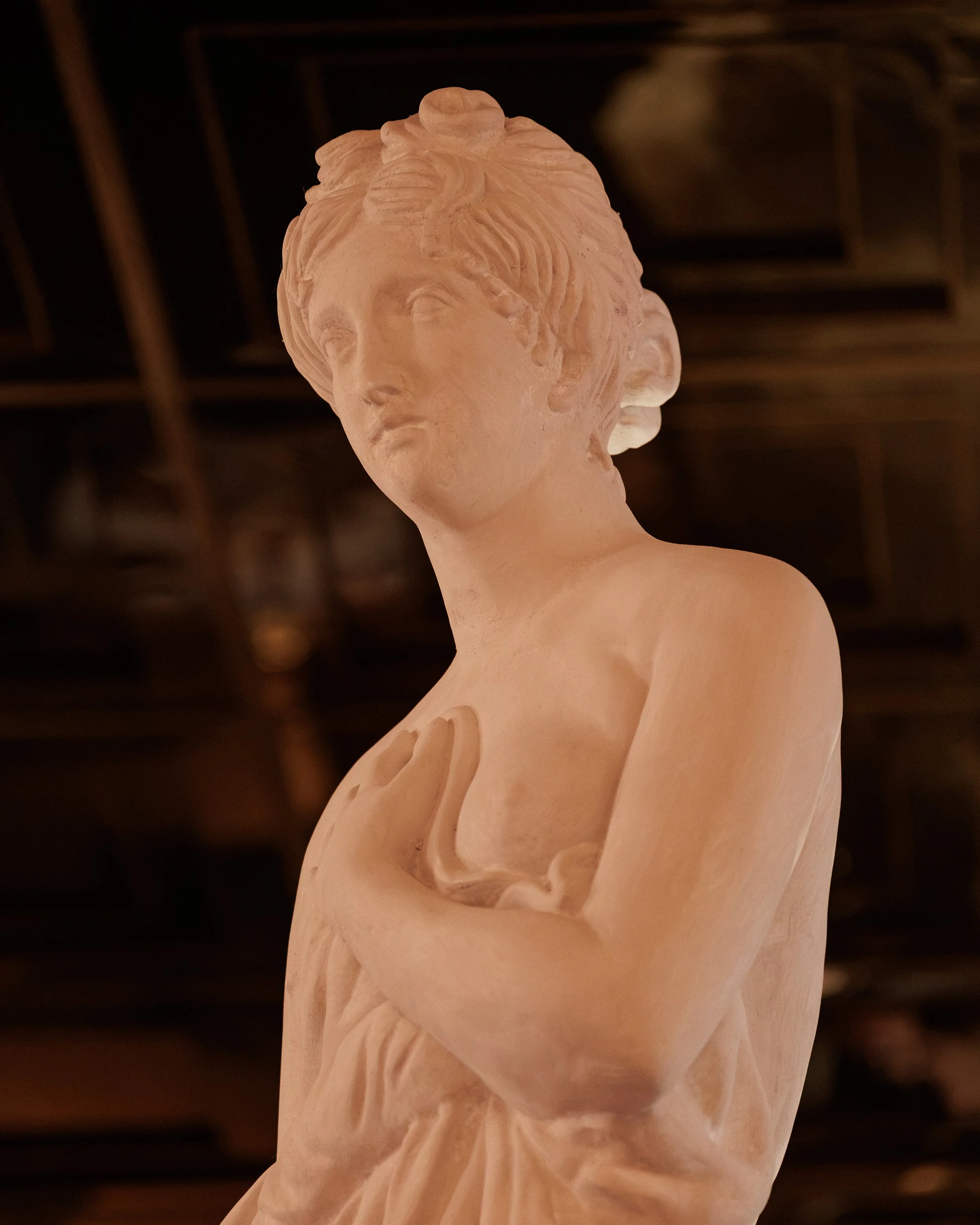 Close-up of a pale classical female statue illuminated by warm, dramatic lighting at Roman God of Fire.