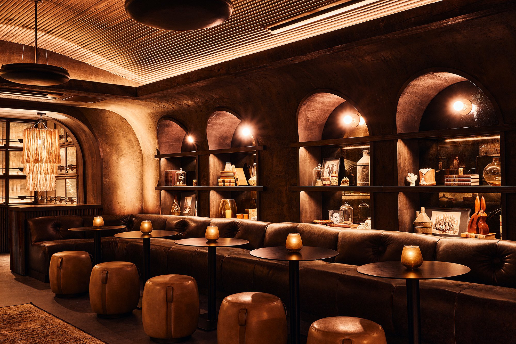 Bar and lounge at dLeña ROJA in Washington, D.C., featuring an illuminated arched spirits display, leather barstools, dark wood finishes and a sculptural ceiling designed by PETERMAX Co.