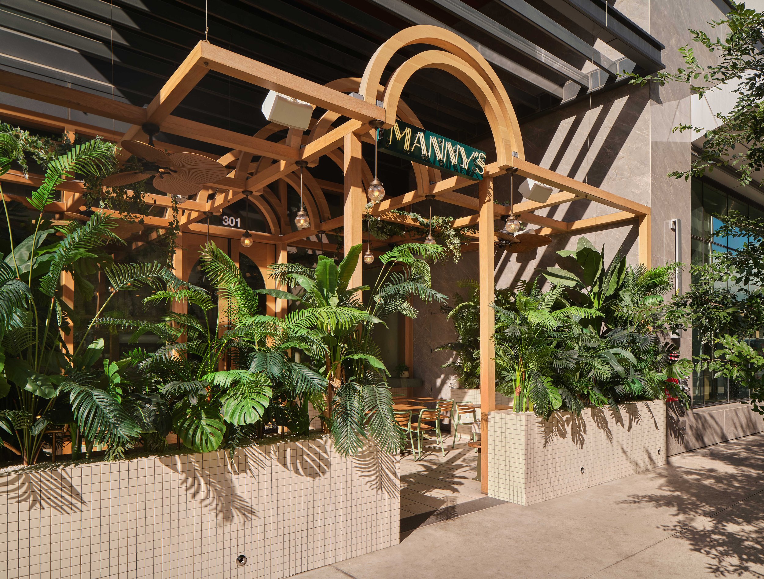 Manny’s and Powder Room entrance in Downtown Austin framed by lush greenery, wood detailing, and a tiled planter wall.