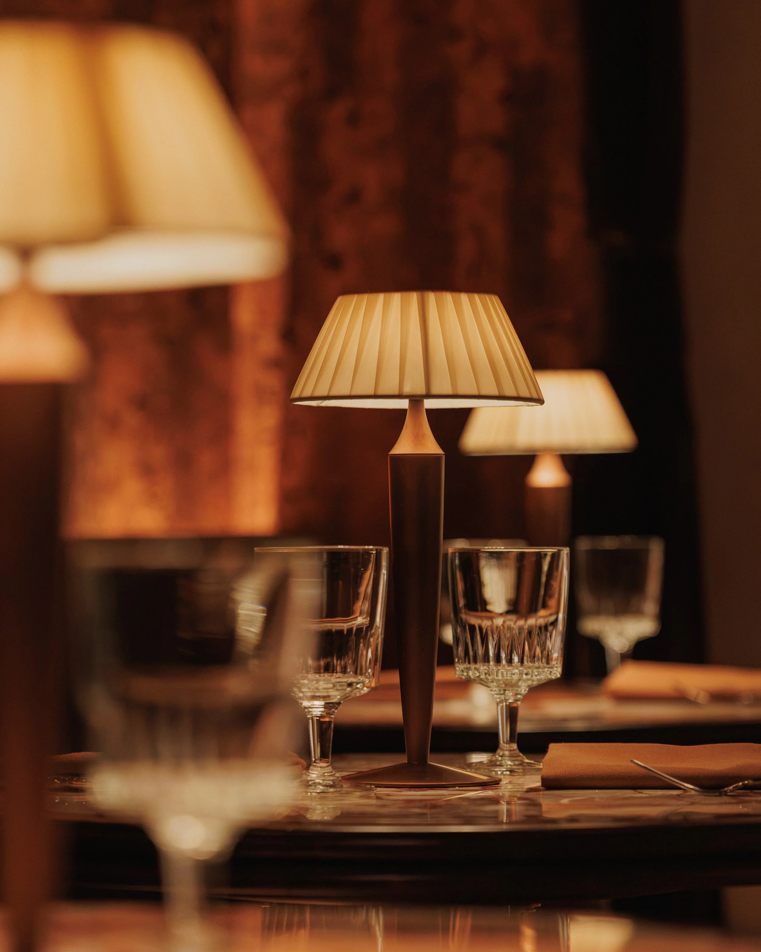 Pleated table lamp illuminating crystal glassware and a formal place setting in the warmly lit Roman God of Fire dining room.