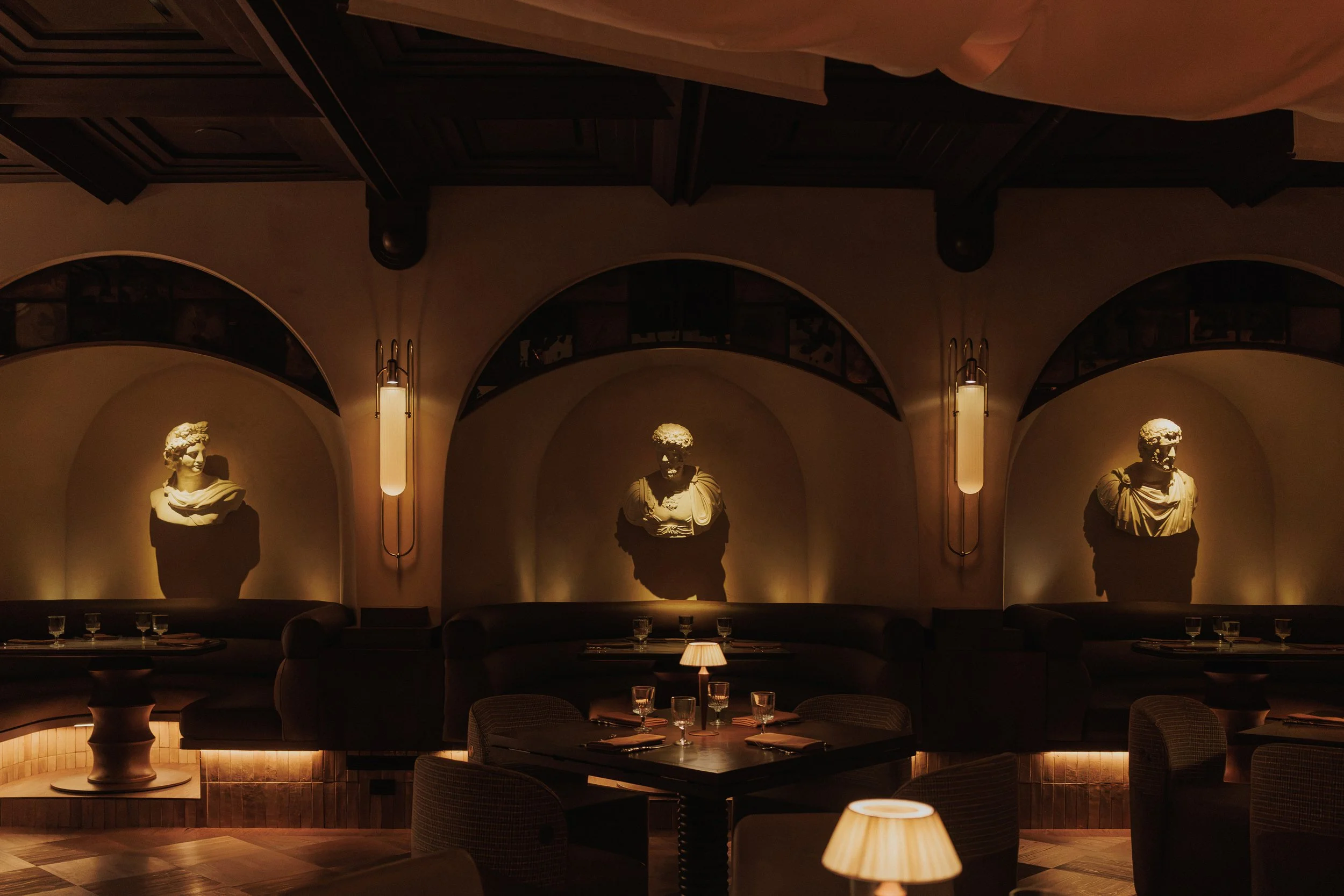 Three illuminated classical busts displayed in arched niches above curved banquette seating at Roman God of Fire.