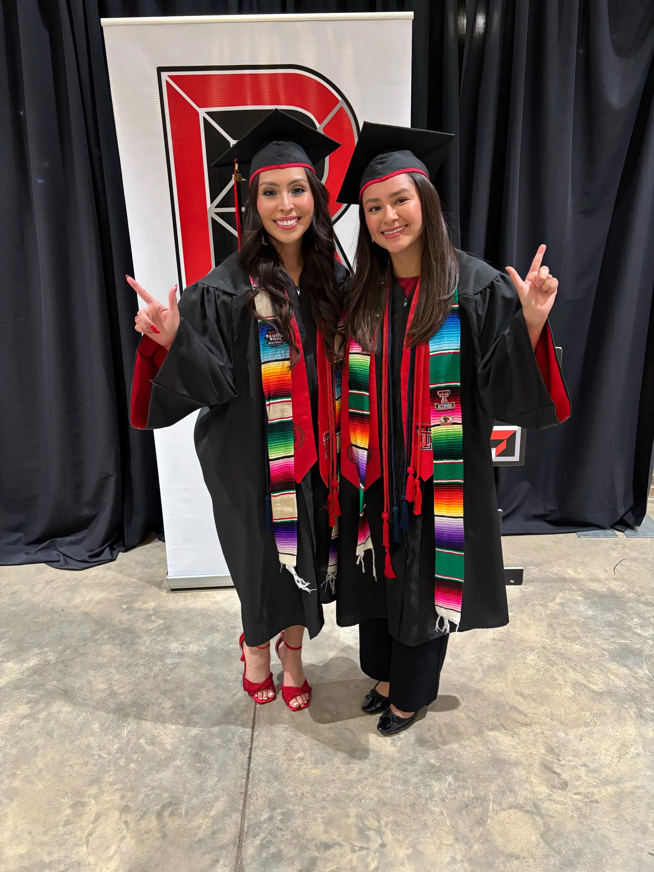 Group of graduates in cap and gown at commencement ceremony, holding red and white carnations, smiling and posing together.