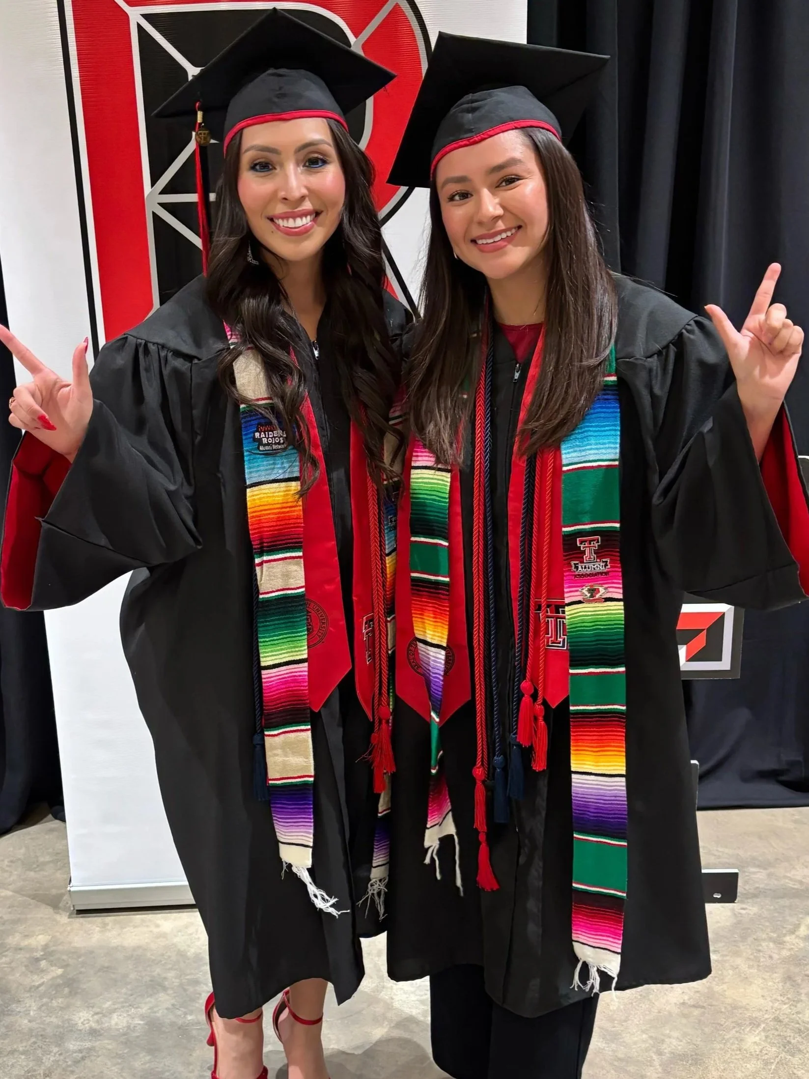 Group of graduates in cap and gown at commencement ceremony, holding red and white carnations, smiling and posing together.