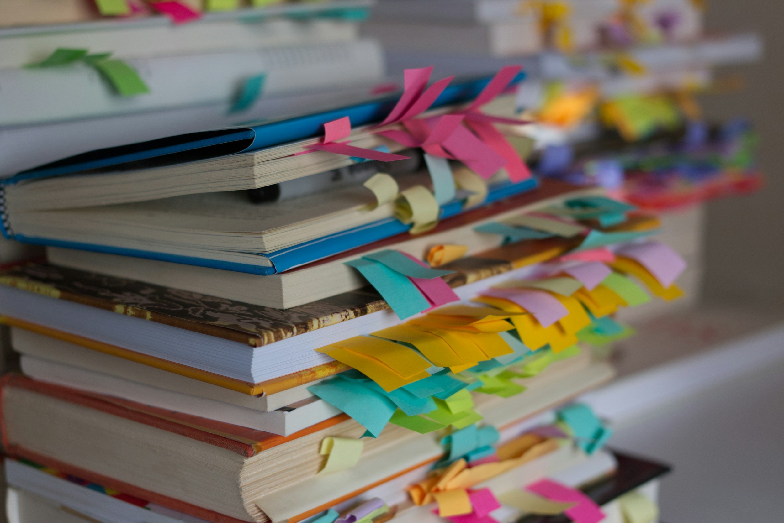 Close-up of a stack of books with colorful sticky notes and flags inserted between the pages for annotating or marking important sections.