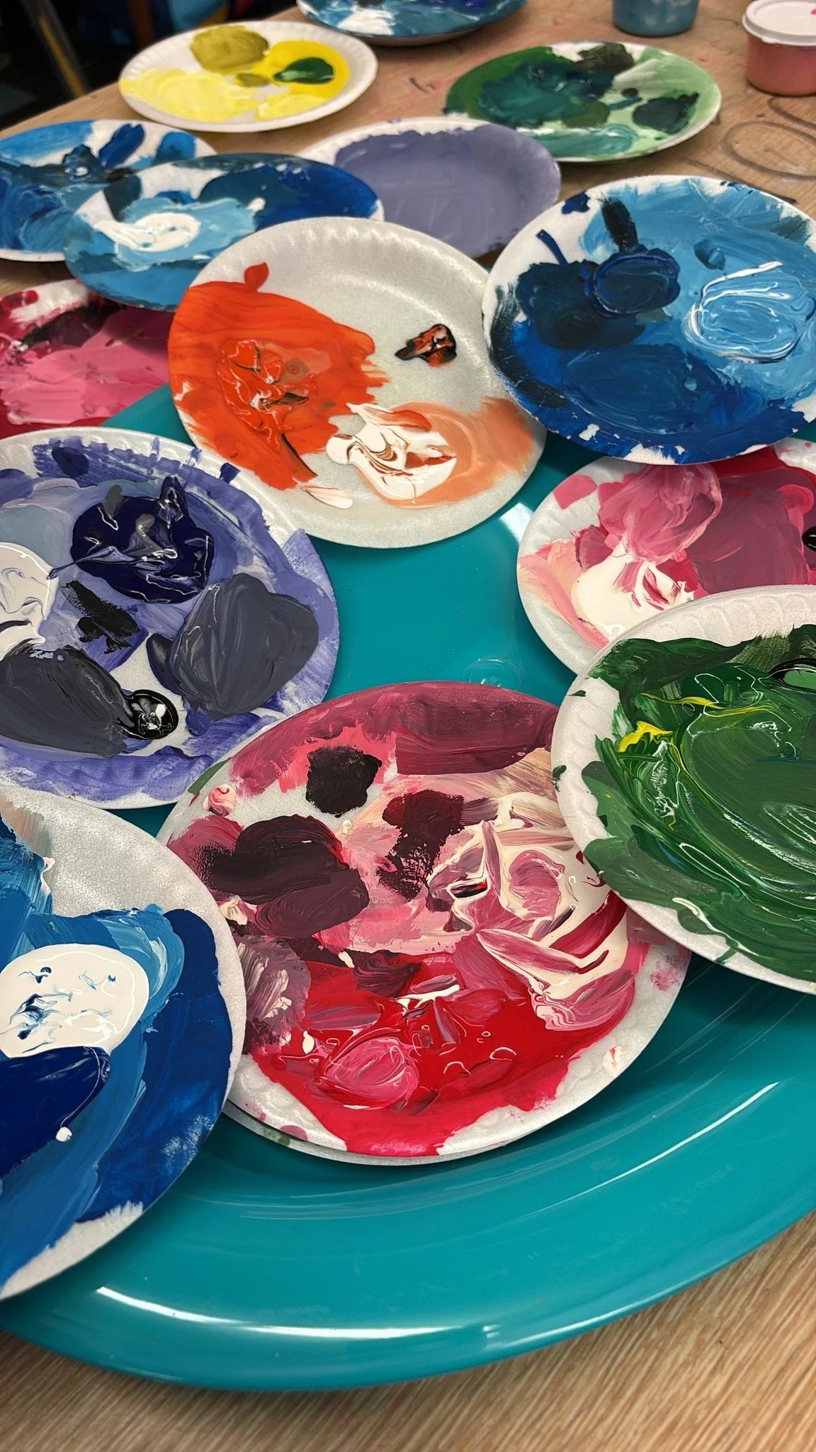 Several paint palettes with various colors of paint, including blue, red, pink, green, yellow, purple, and black, arranged on a blue tray.