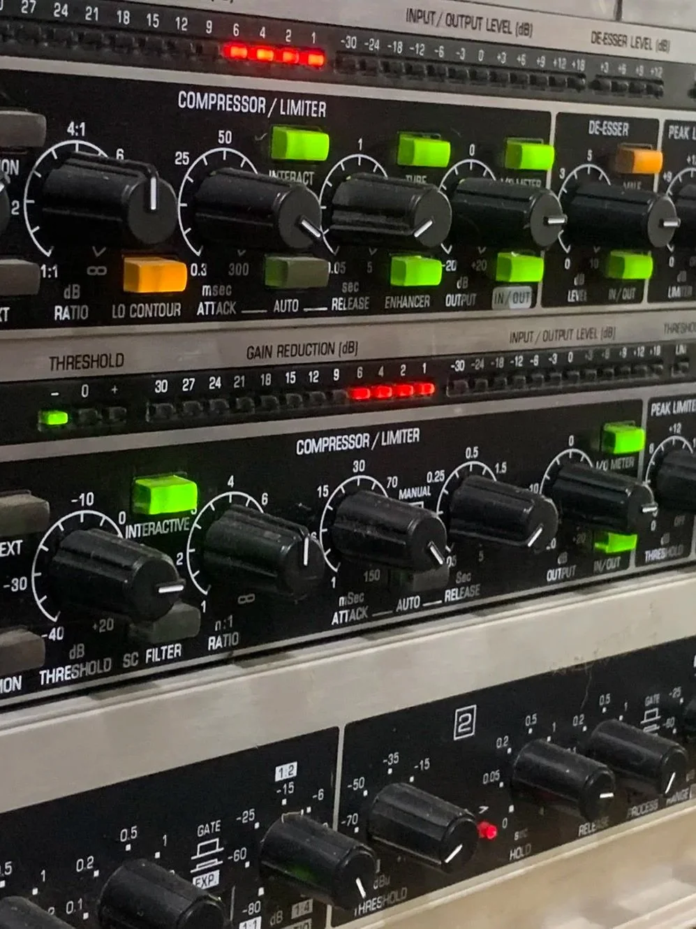 Close-up of audio mixing equipment with various knobs, dials, and sliders, including compressor, limiter, and gain controls, with LED indicator lights.