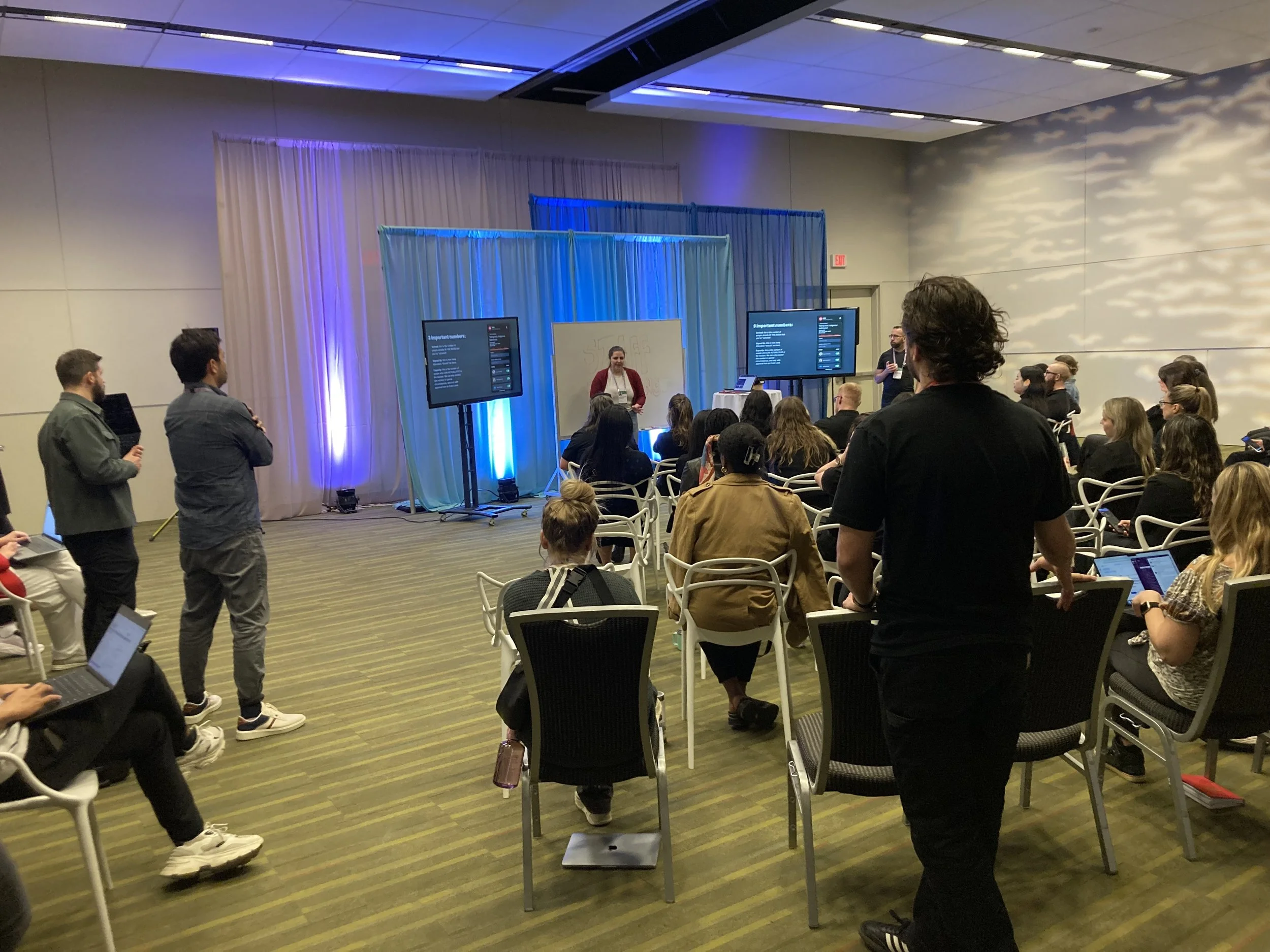 About 20 people in a conference room gathered around a presenter.