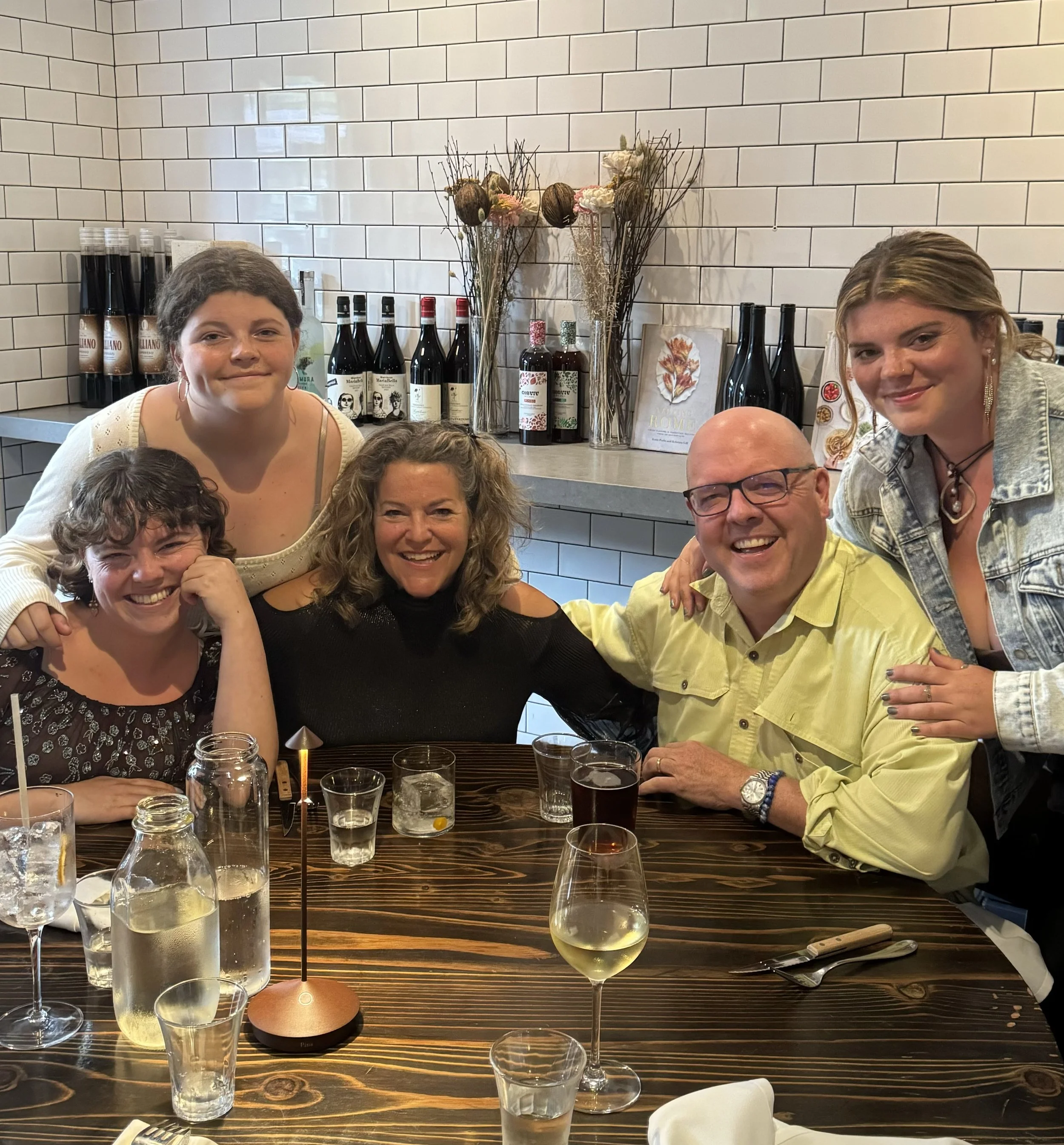 Group of five people smiling and enjoying drinks at a restaurant table.