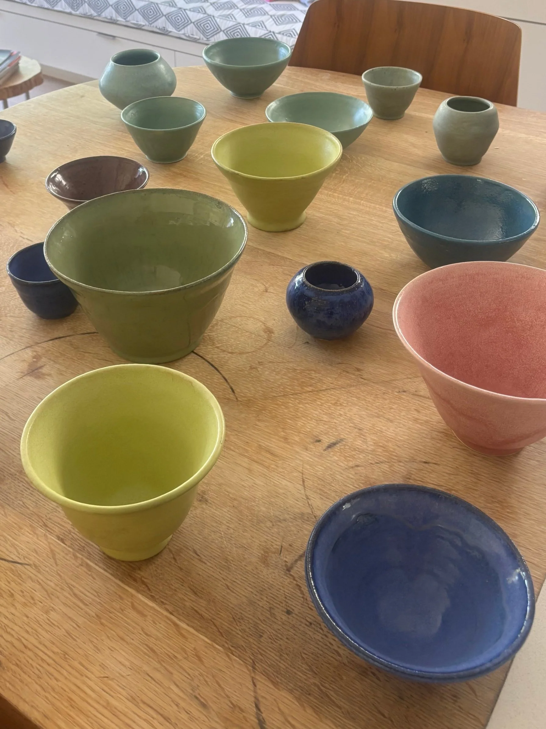 Multiple colorful ceramic bowls and vases on a wooden table.