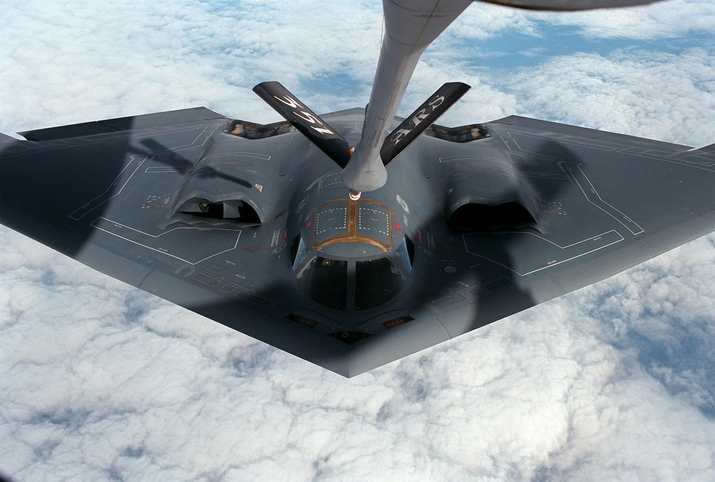 F-22 fighter jet flying high above clouds, viewed from below.