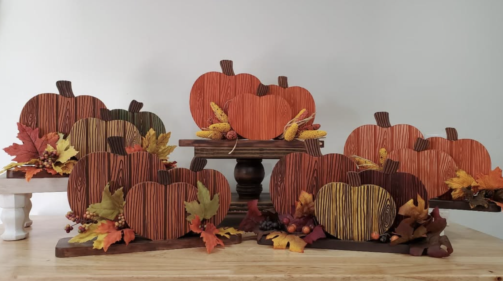 Autumn-themed pumpkin decorations featuring wooden pumpkins, colorful fall leaves, and berries displayed on wooden surfaces.