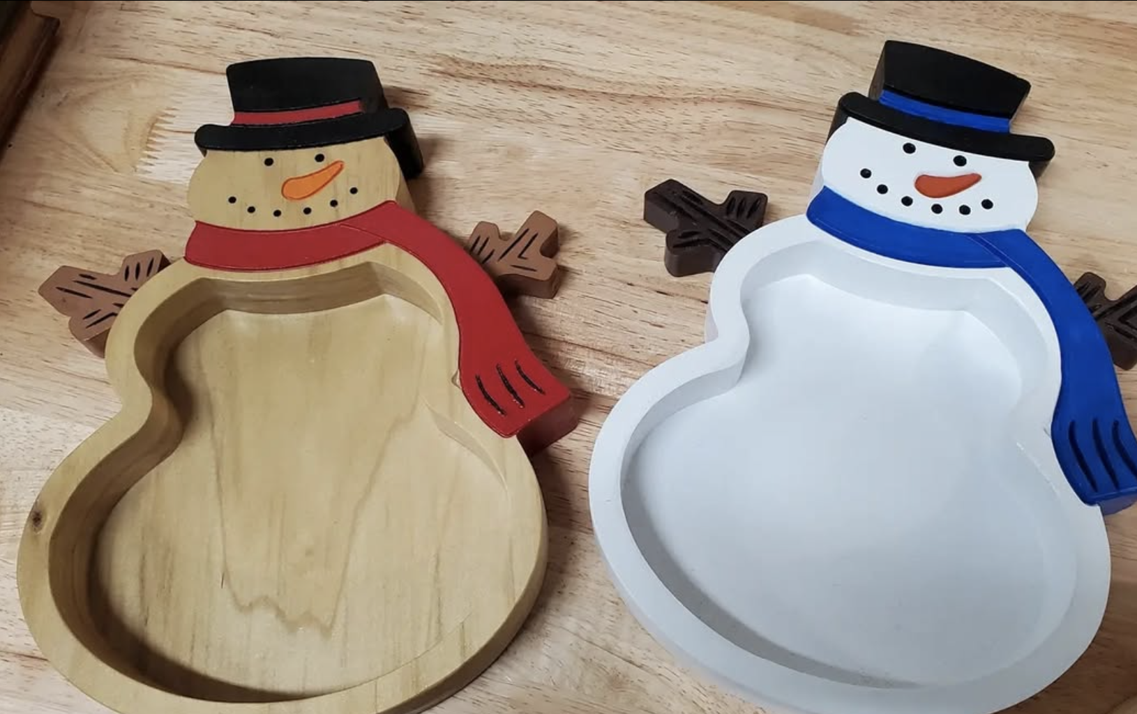 Snowman-shaped cookie or treat mold decorated with a black top hat, black dots, an orange carrot nose, and a red or blue scarf, with the mold's interior visible in the same shape.