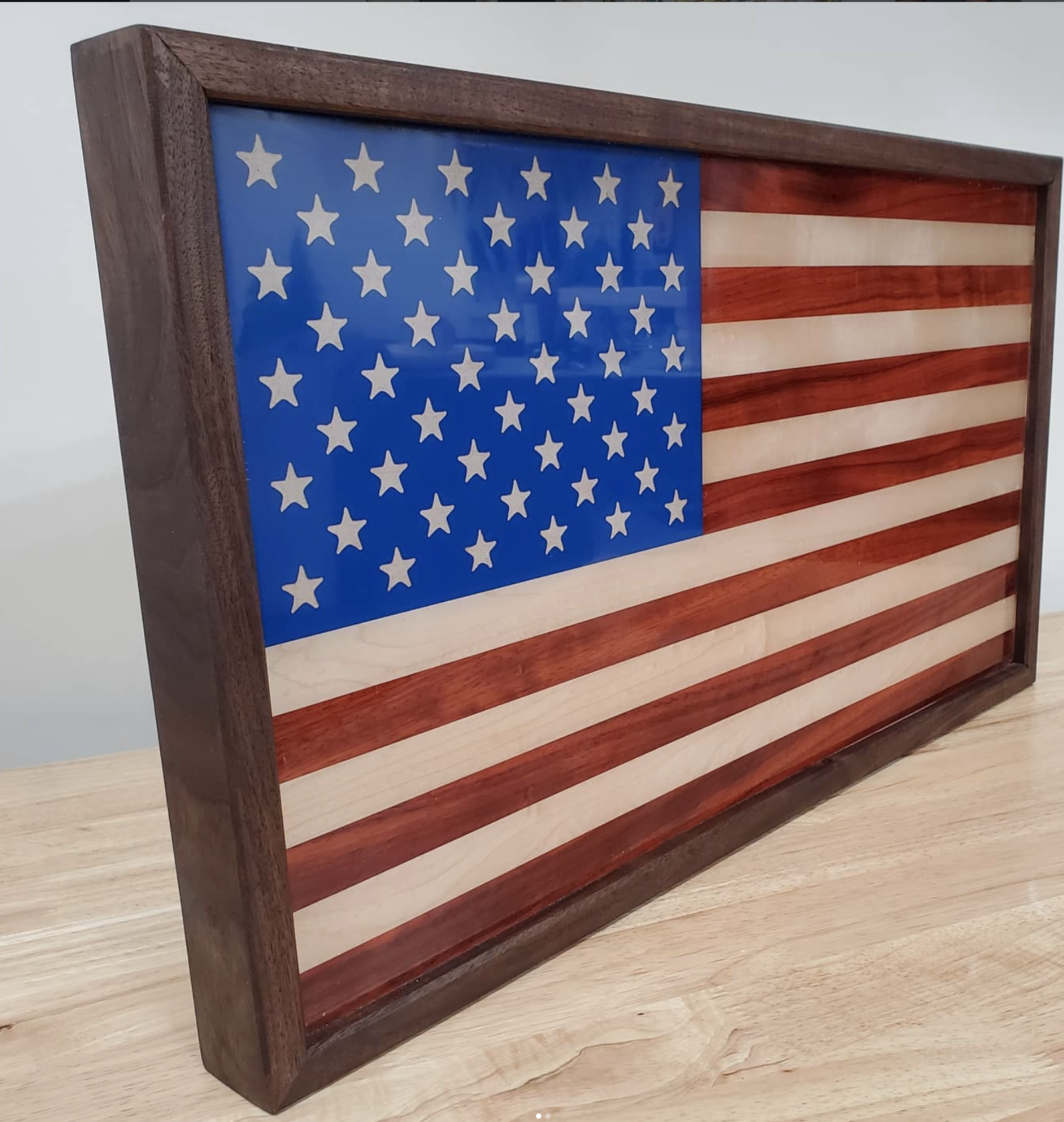 A wooden cutting board featuring an American flag with a blue canton and white stars on the left and red and white stripes on the right.
