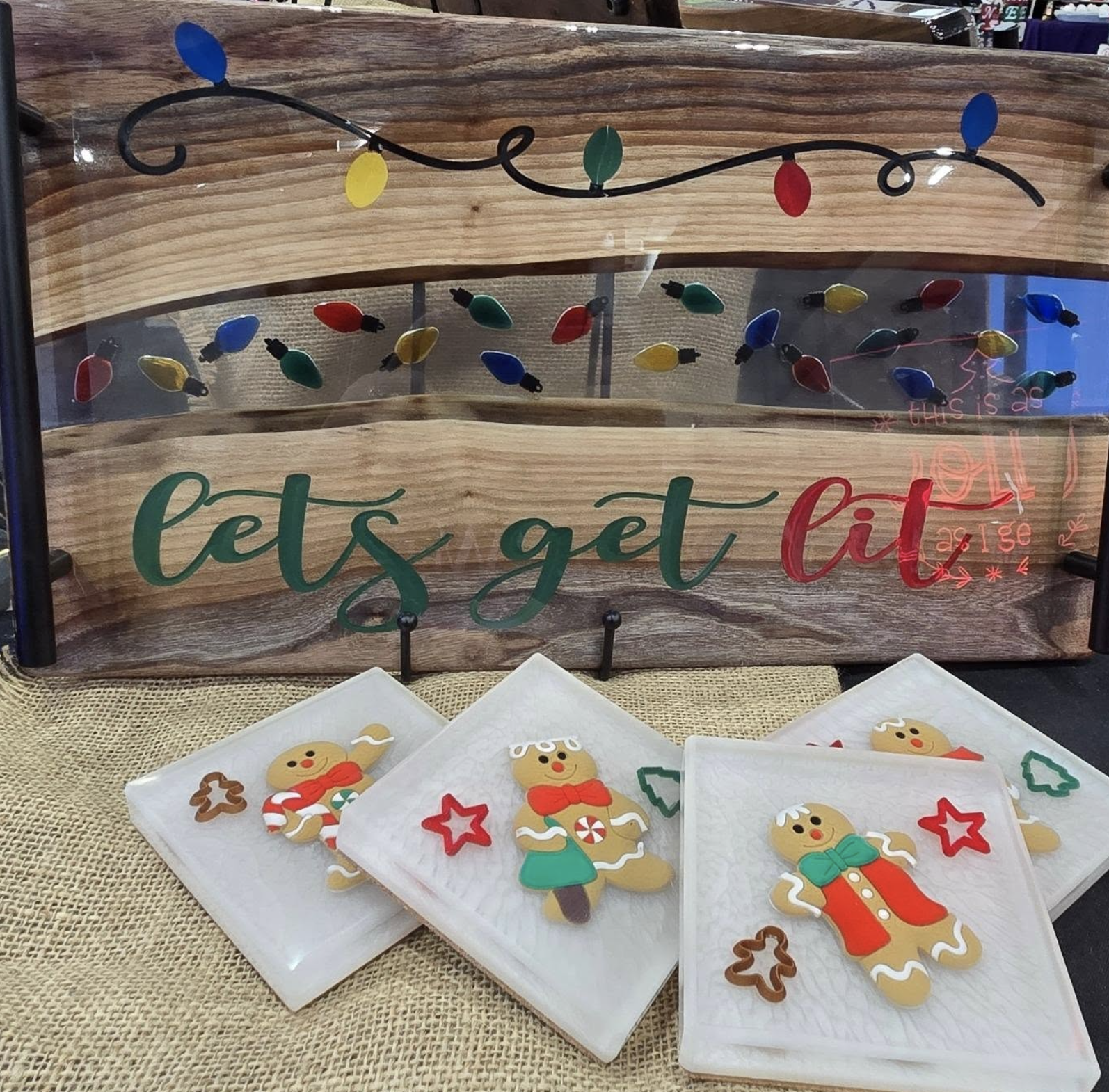 Christmas-themed cookies decorated as gingerbread people and holiday symbols, displayed on white plates with a wooden sign in the background that says 'let's get lit' and features colorful holiday lights.