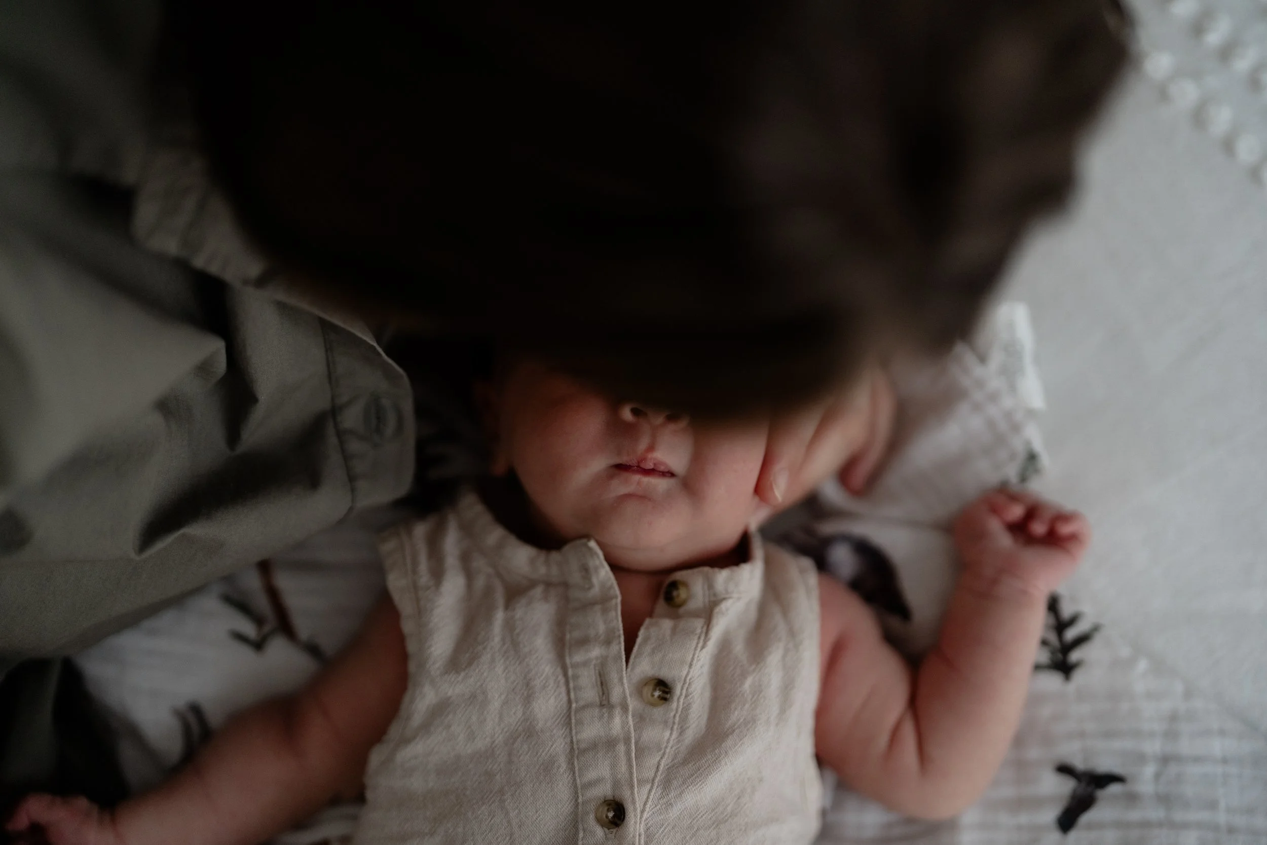 Close-up of a newborn baby sleeping on a patterned pillow, with an adult's face gently resting near the baby's head.