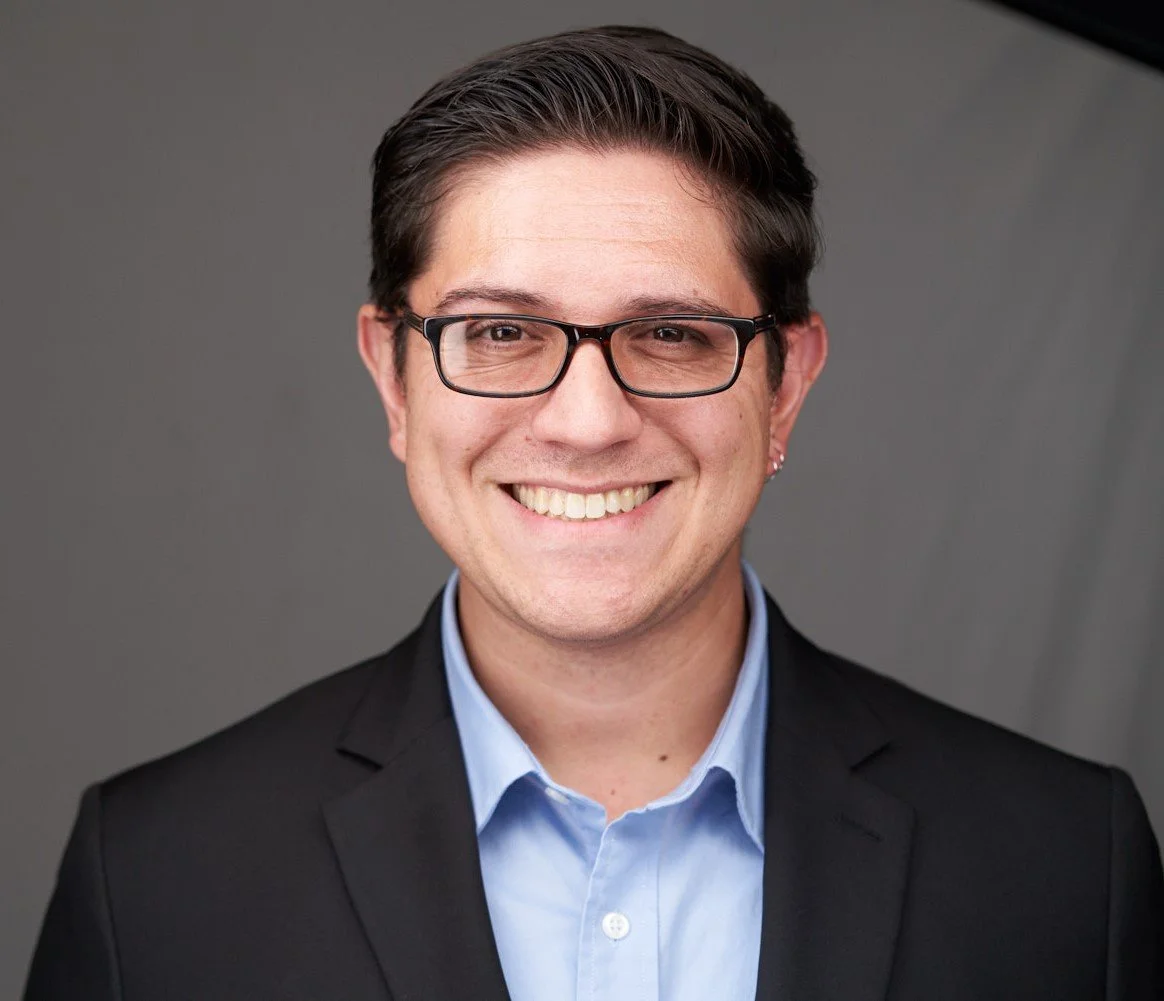 Headshot photo of Trusted Communications, LLC partner Will Powell, a white man wearing a black suit with blue button down shirt, and glasses.