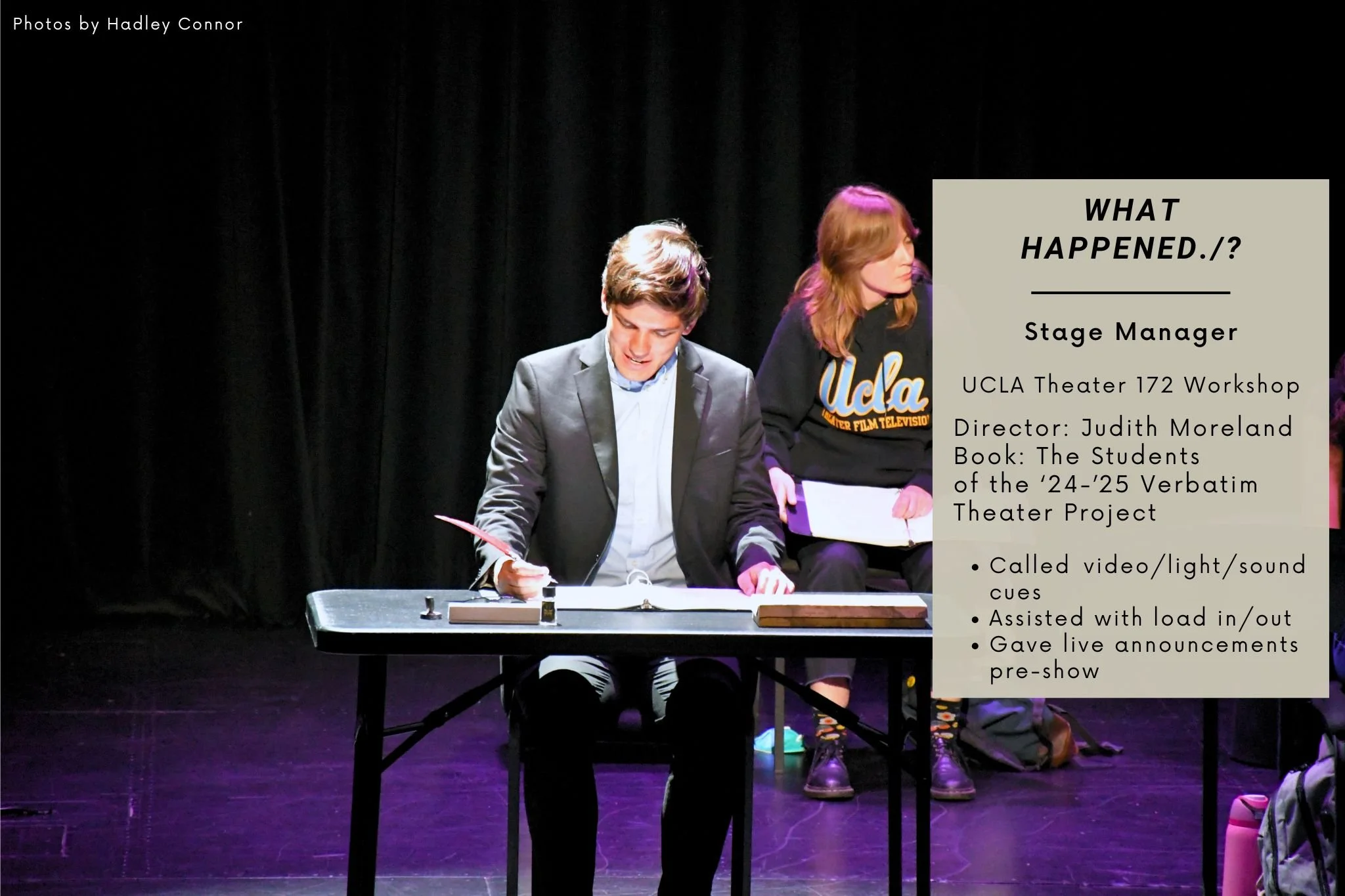 Two people sitting at a table on stage, one man and one woman, participating in a theater workshop. The man is writing on paper, dressed in a suit, while the woman is looking to the side, wearing a UCLA sweatshirt. The stage background is black.