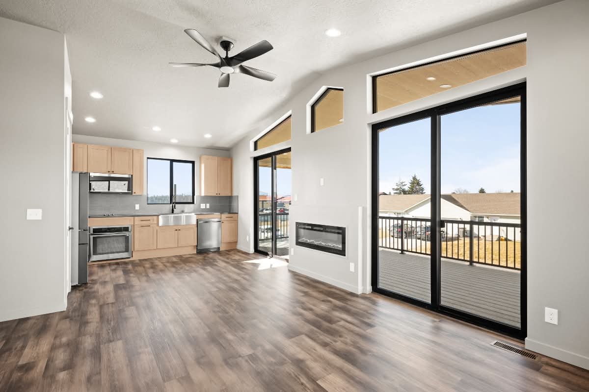Open-concept living room with a kitchen area, large sliding glass doors leading to a balcony, hardwood floors, and a ceiling fan.