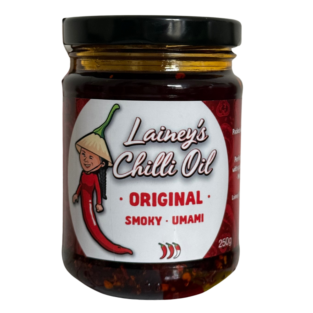 A jar of Lainey's Chilli Oil labeled as original, smoky, umami flavor, with a cartoon character of a smiling girl wearing a traditional Asian conical hat and a red dress, standing next to a red chili pepper.